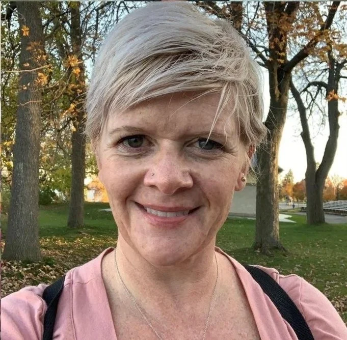 A woman is short blonde hair surrounded by nature