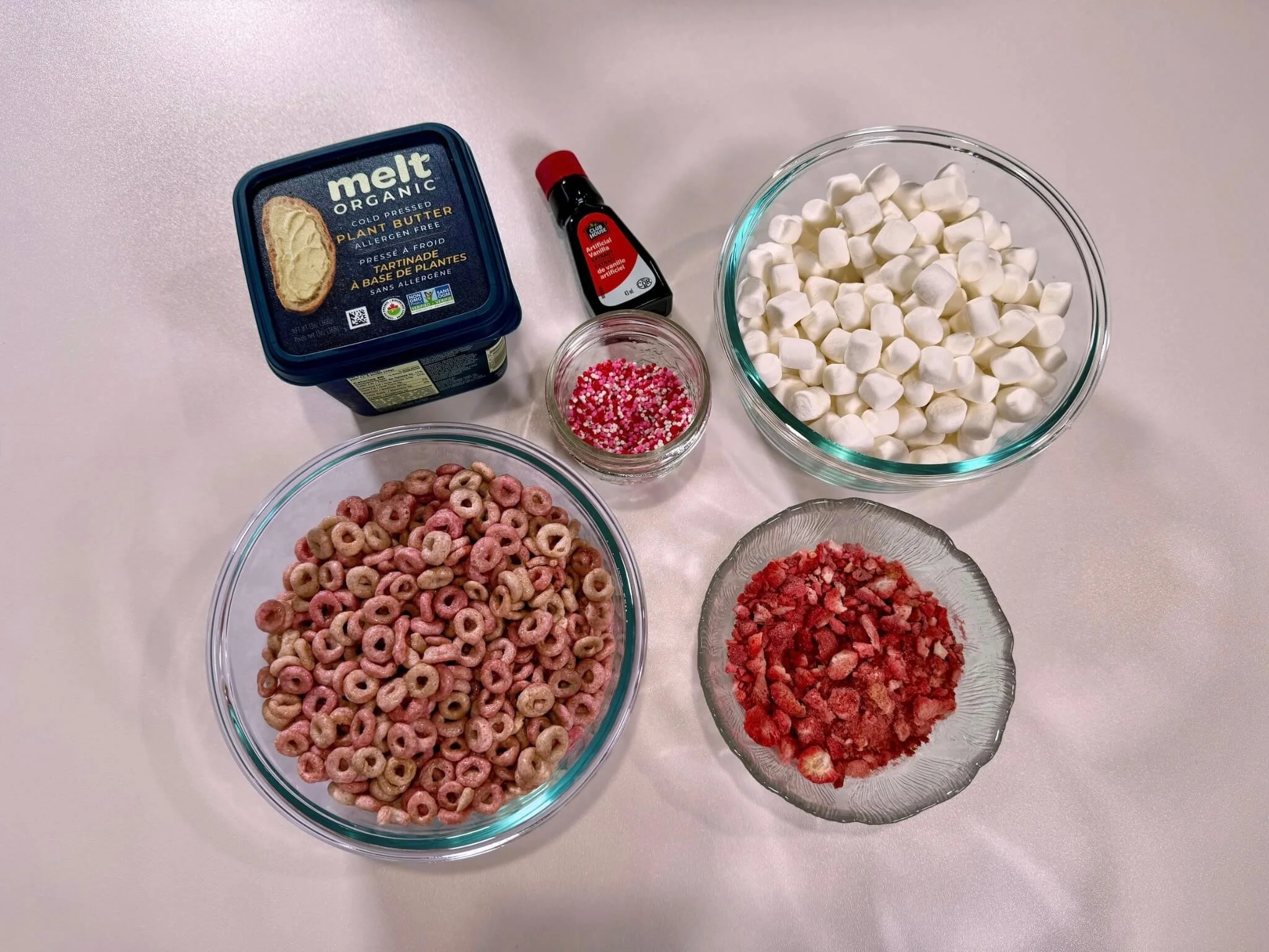 a table full of ingredients that includes cereal, butter, sprinkles, marshmallows and crushed strawberries