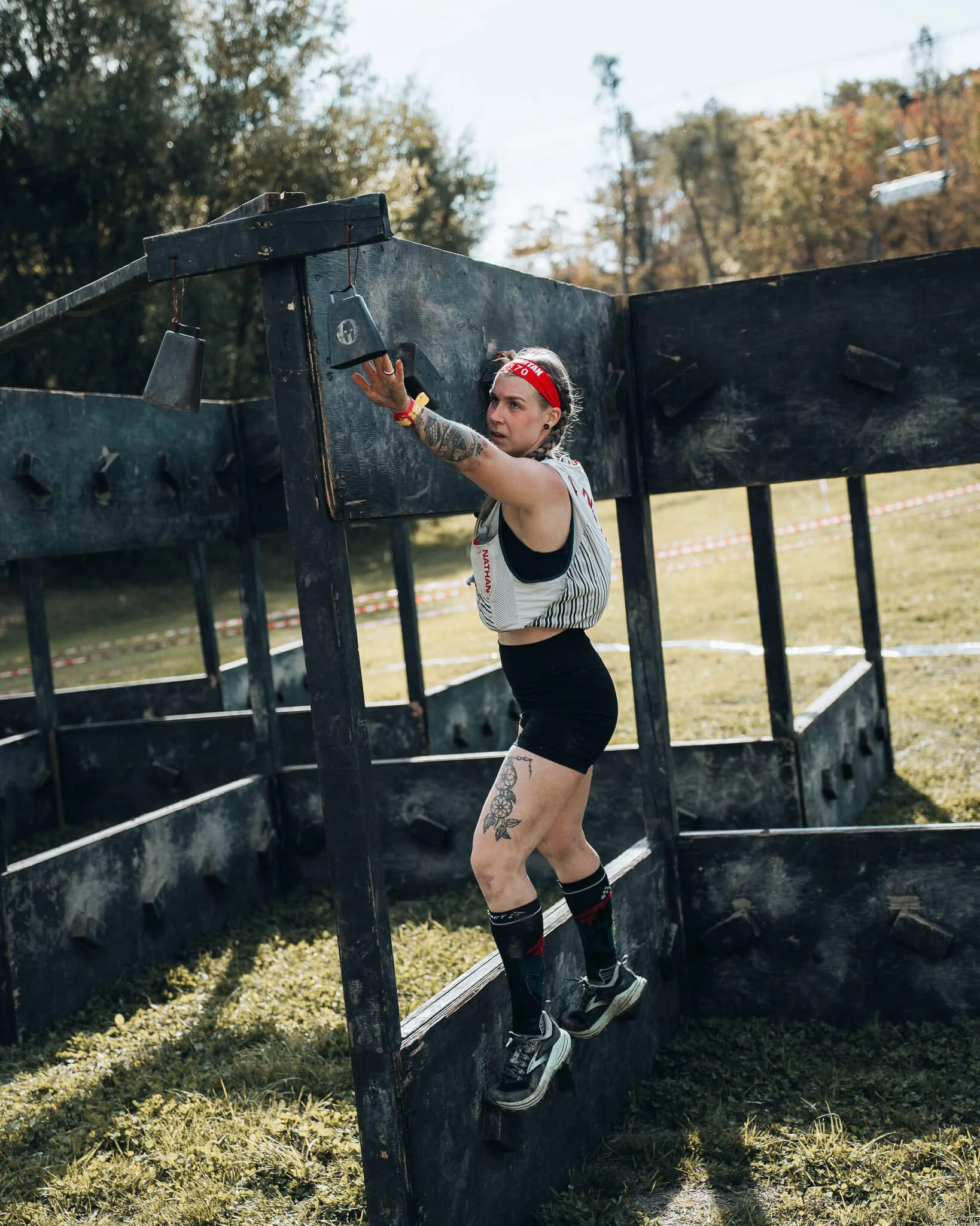 Woman with a red headband and running clothes on is ringing a bell on an obstacle at a spartan race