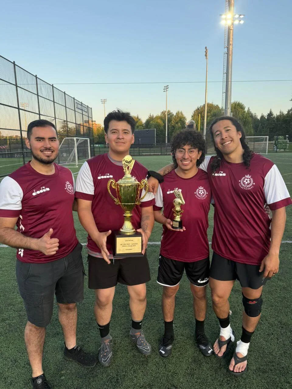 Four Soccer players hold up a championship trophy at a soccer field
