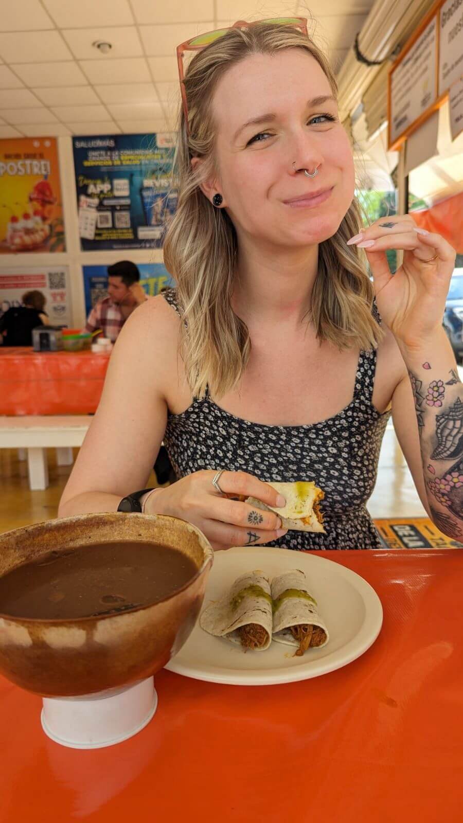 a woman in eating tacos and drinking a brown drink at a brightly coloured restaurant