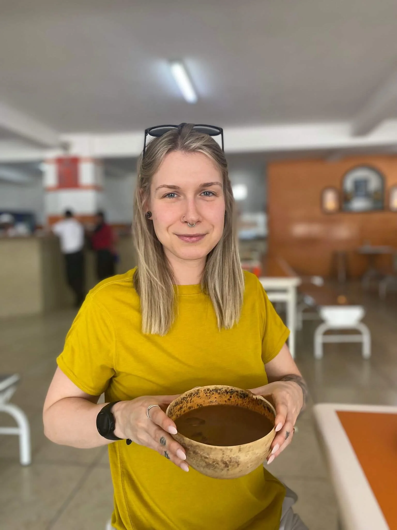 a blonde woman holds a bowl of pozol in a restaurant