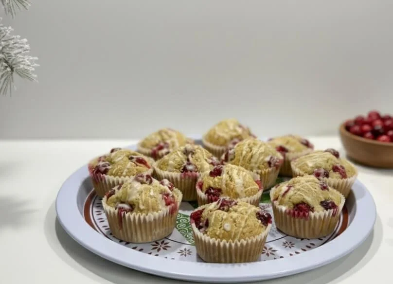 Orange Cranberry Muffins on a christmas plate with some white frosted garland and a bowl of cranberries in the background