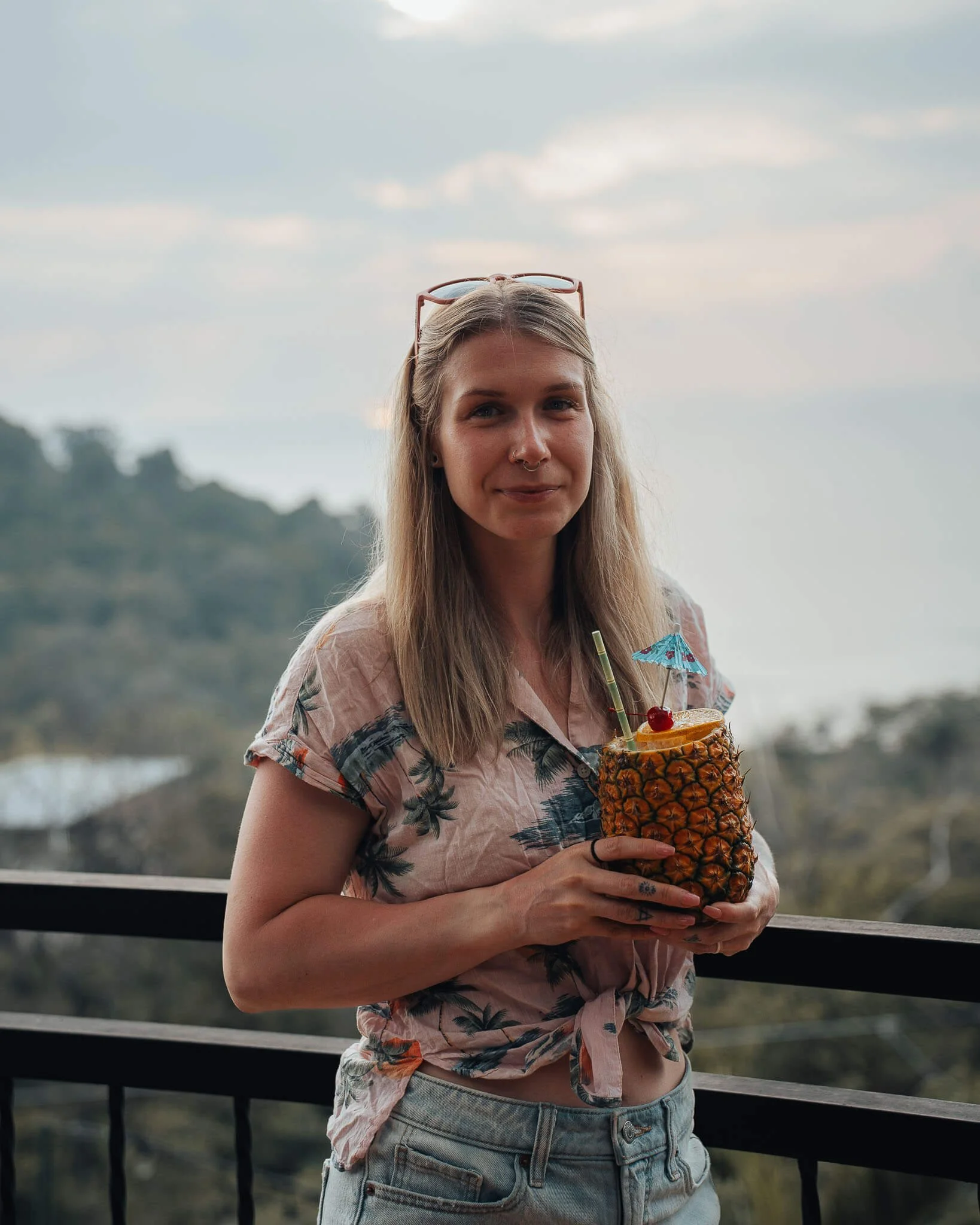 woman is standing and holding a pineapple in her hand that has a drink in it
