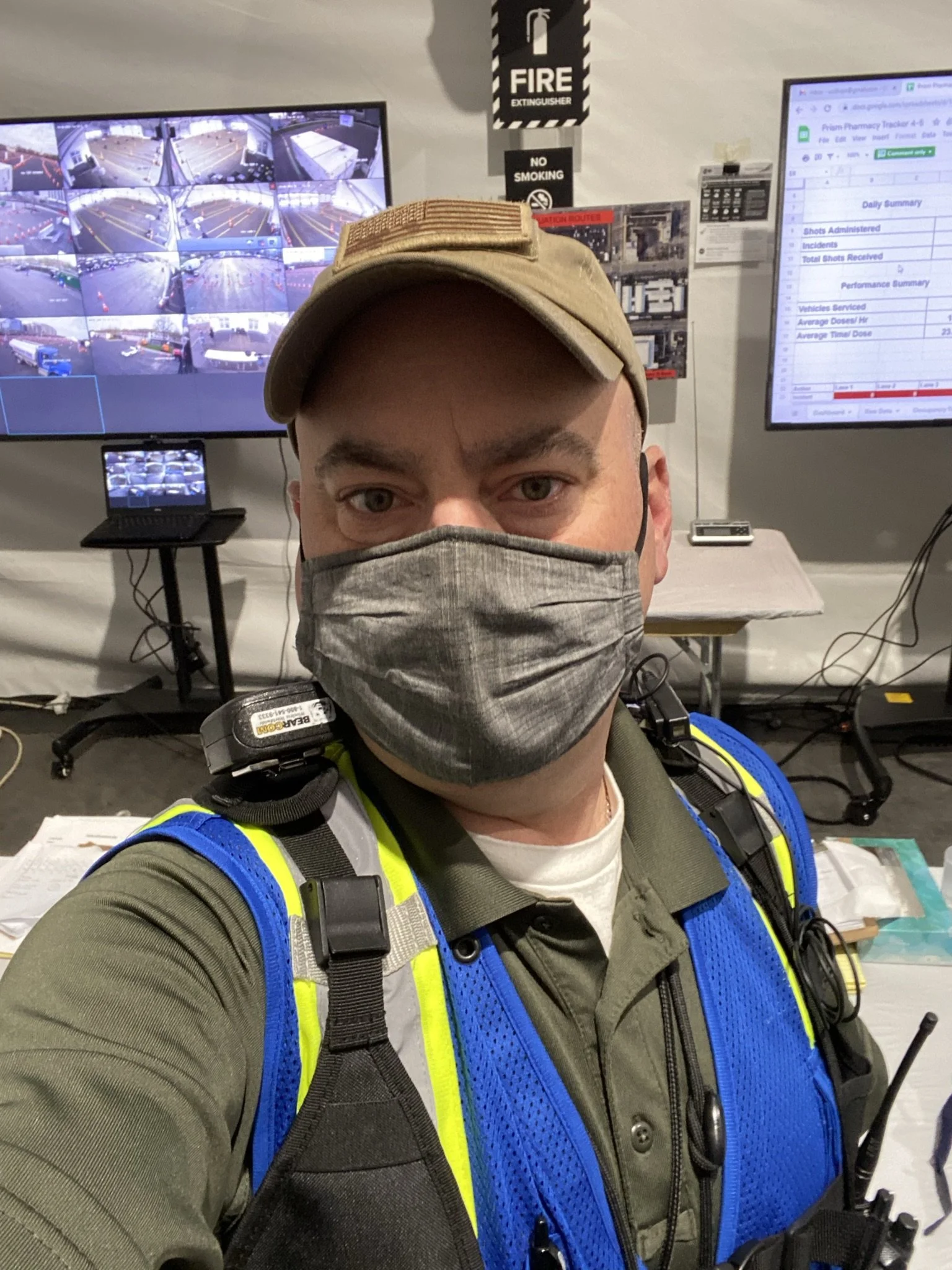 Consultant wearing a mask and vest, standing in a command center during COVID, 2020.