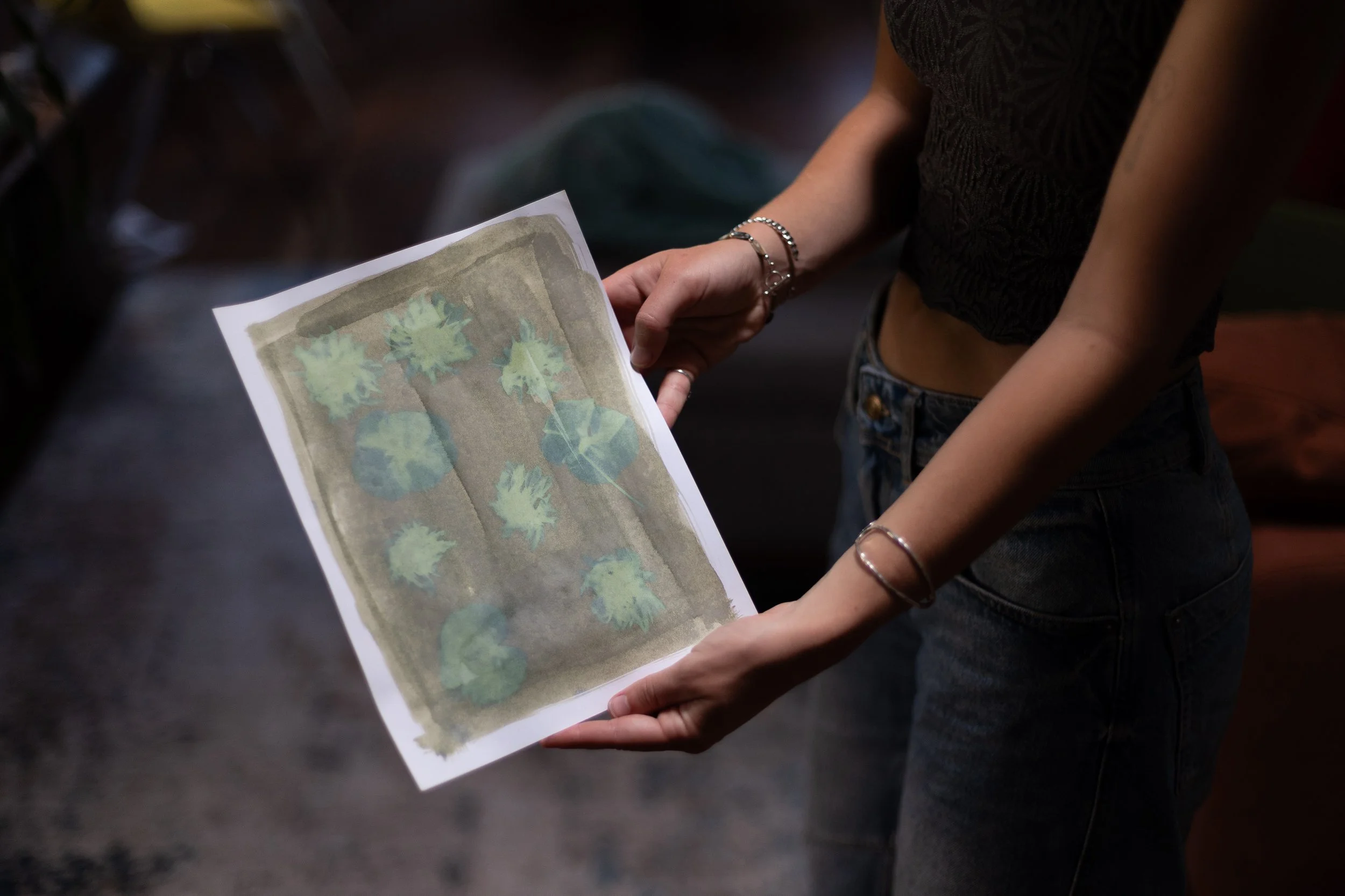 Person holding a sheet of paper with leaf and plant illustrations, wearing dark jeans and a black top with short sleeves.