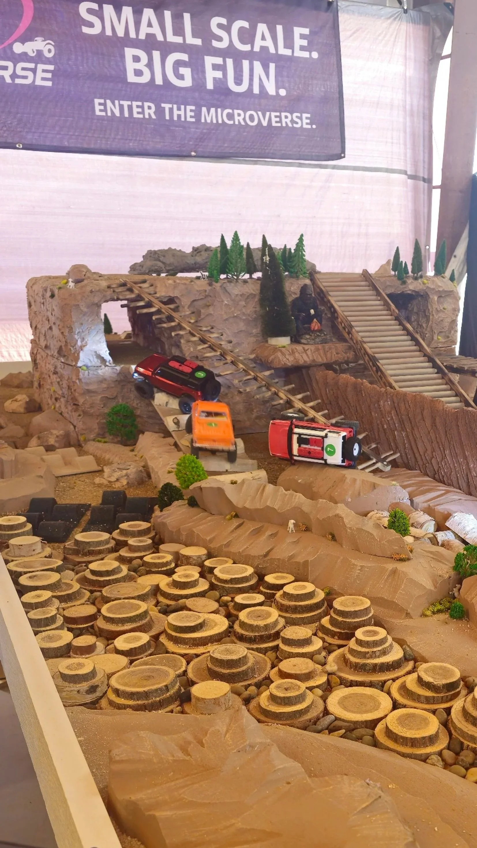 Miniature mountain landscape with toy trucks, trees, and a train track, set up as a model or diorama.