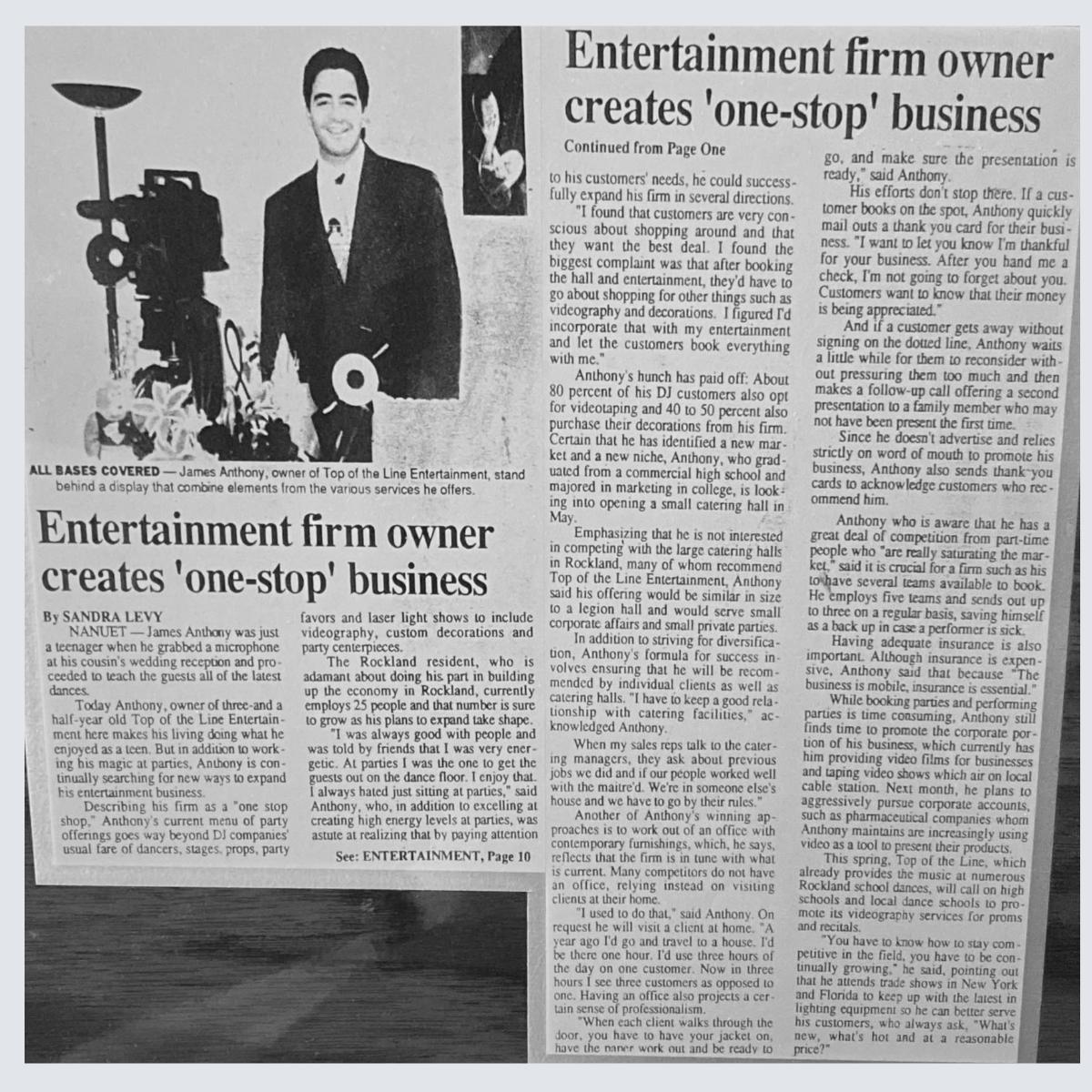 Black and white newspaper article featuring James Anthony, owner of Top of the Line Entertainment, with a photo of him standing behind a display of event elements such as a camera, flowers, and party decor. The article discusses his entertainment business creating a one-stop service for event needs.