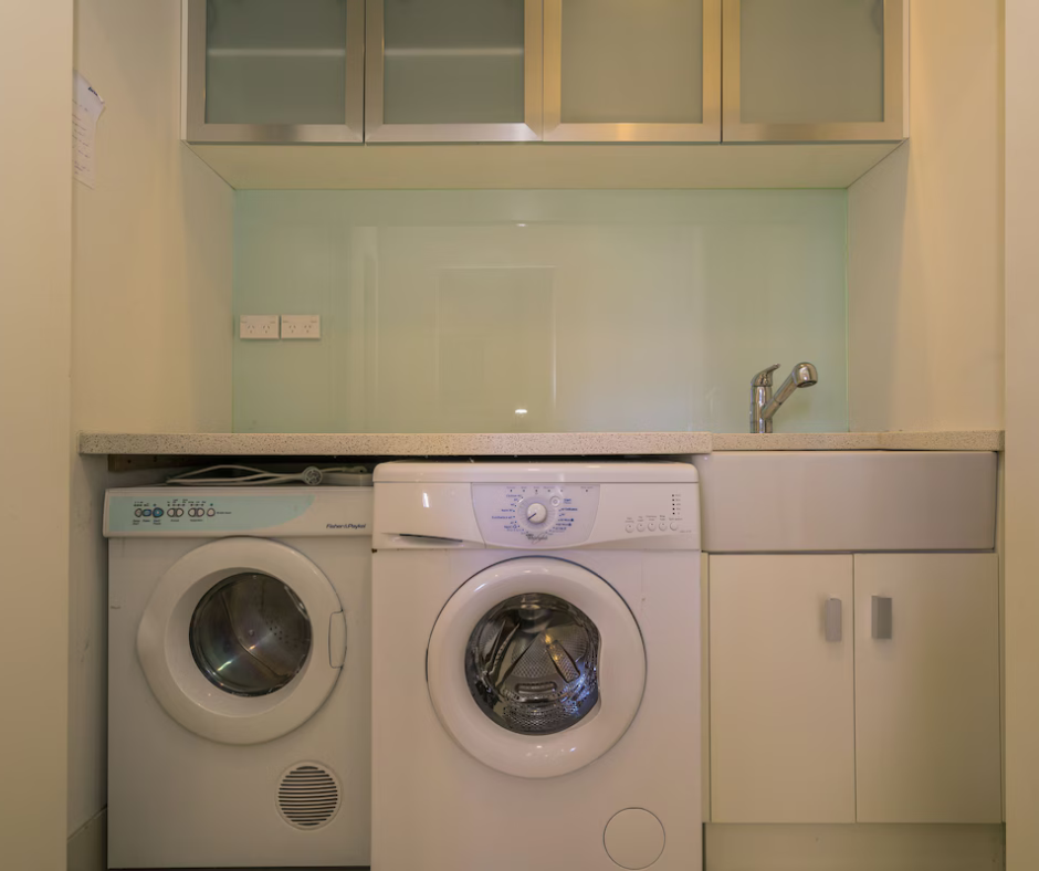 Laundry area with washing machine and dryer below a countertop with a small sink and a faucet, upper cabinets above, and electrical outlets to the left.