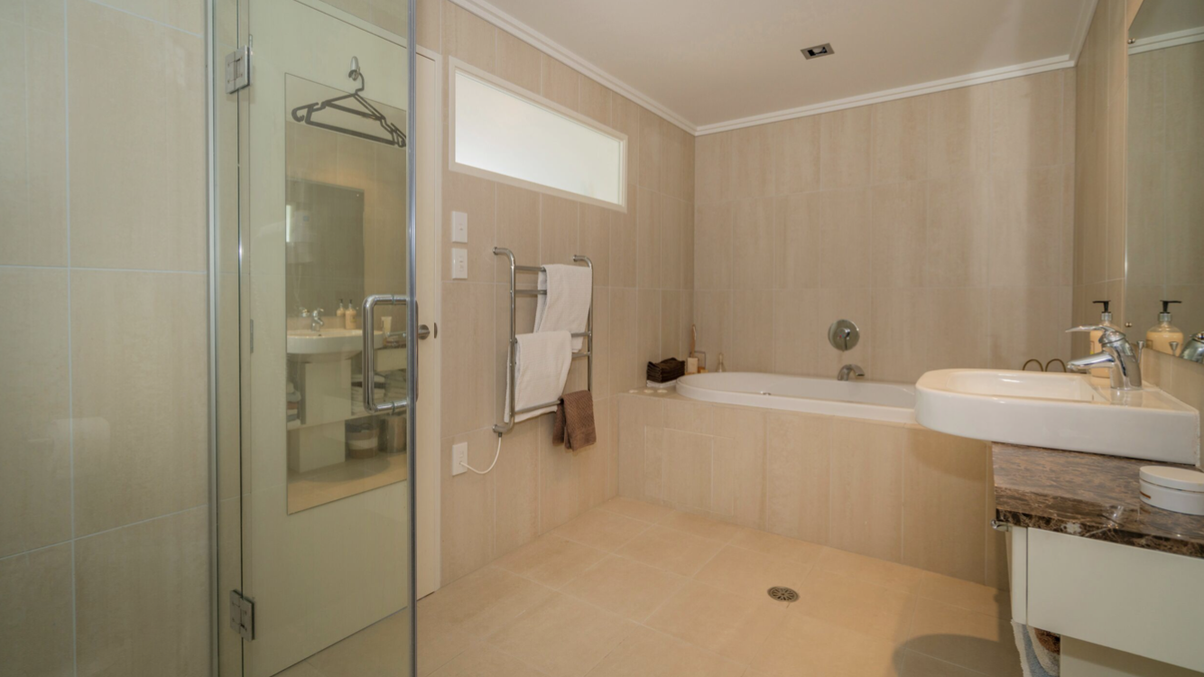 Bathroom with bathtub, sink, glass shower, radiator, and beige tiles.