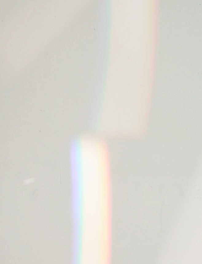A soft, blurry image with faint light refractions creating rainbow-like streaks on a light, neutral background.