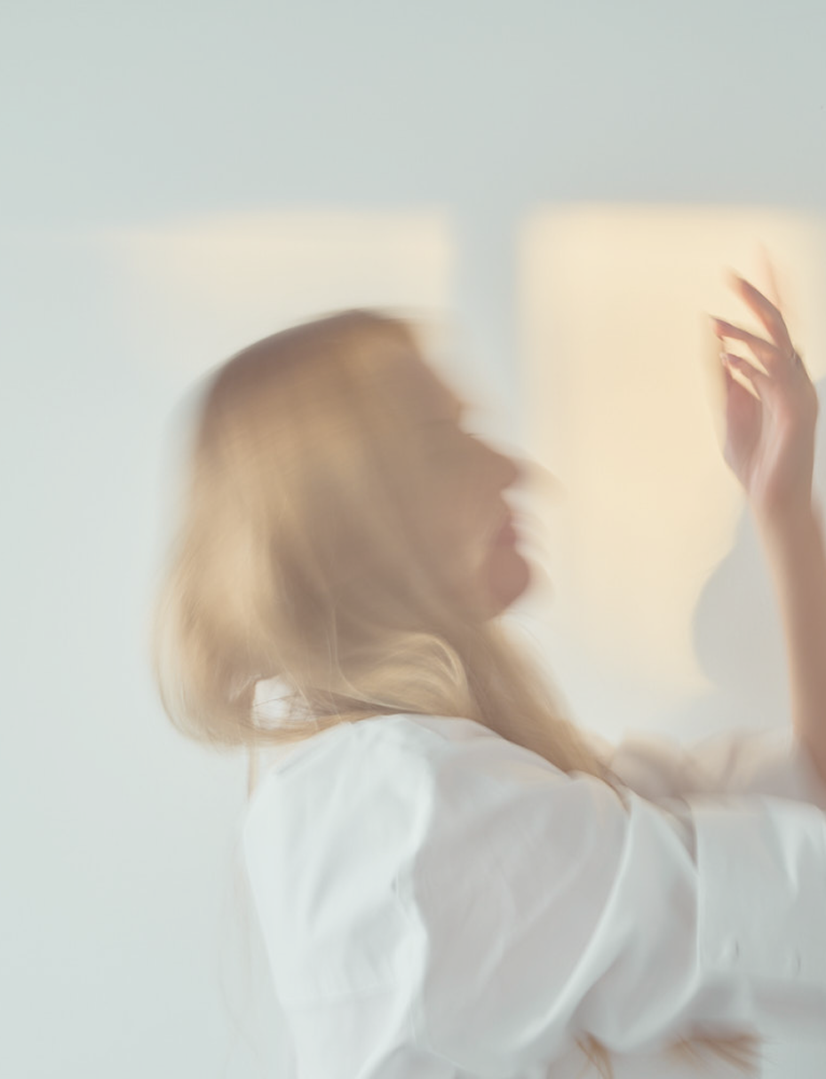 Blurry side profile of a woman with blonde hair touching a frosted glass or window.