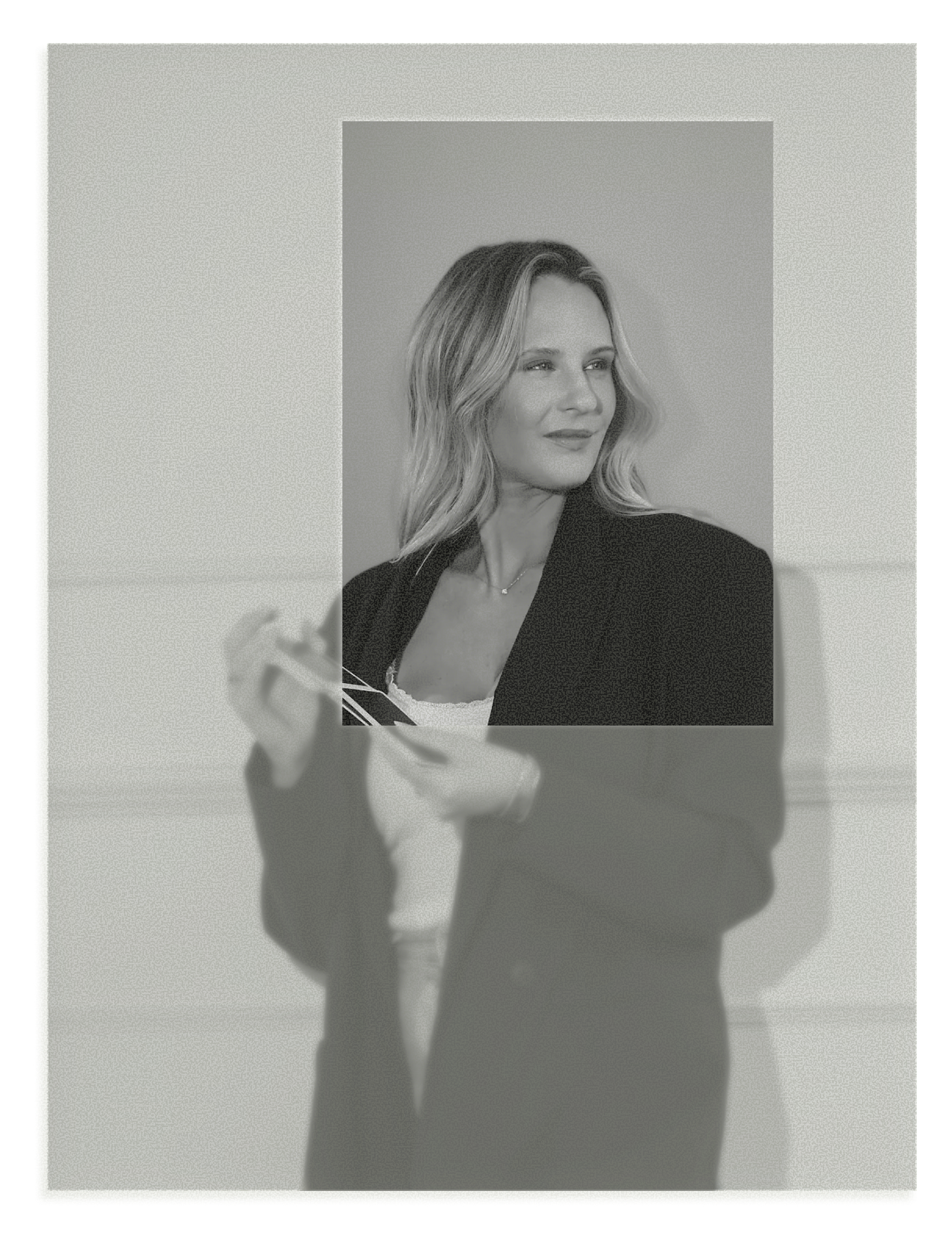 Black and white photo of a woman with shoulder-length wavy hair, wearing a blazer, holding a smartphone, positioned in front of a plain wall.