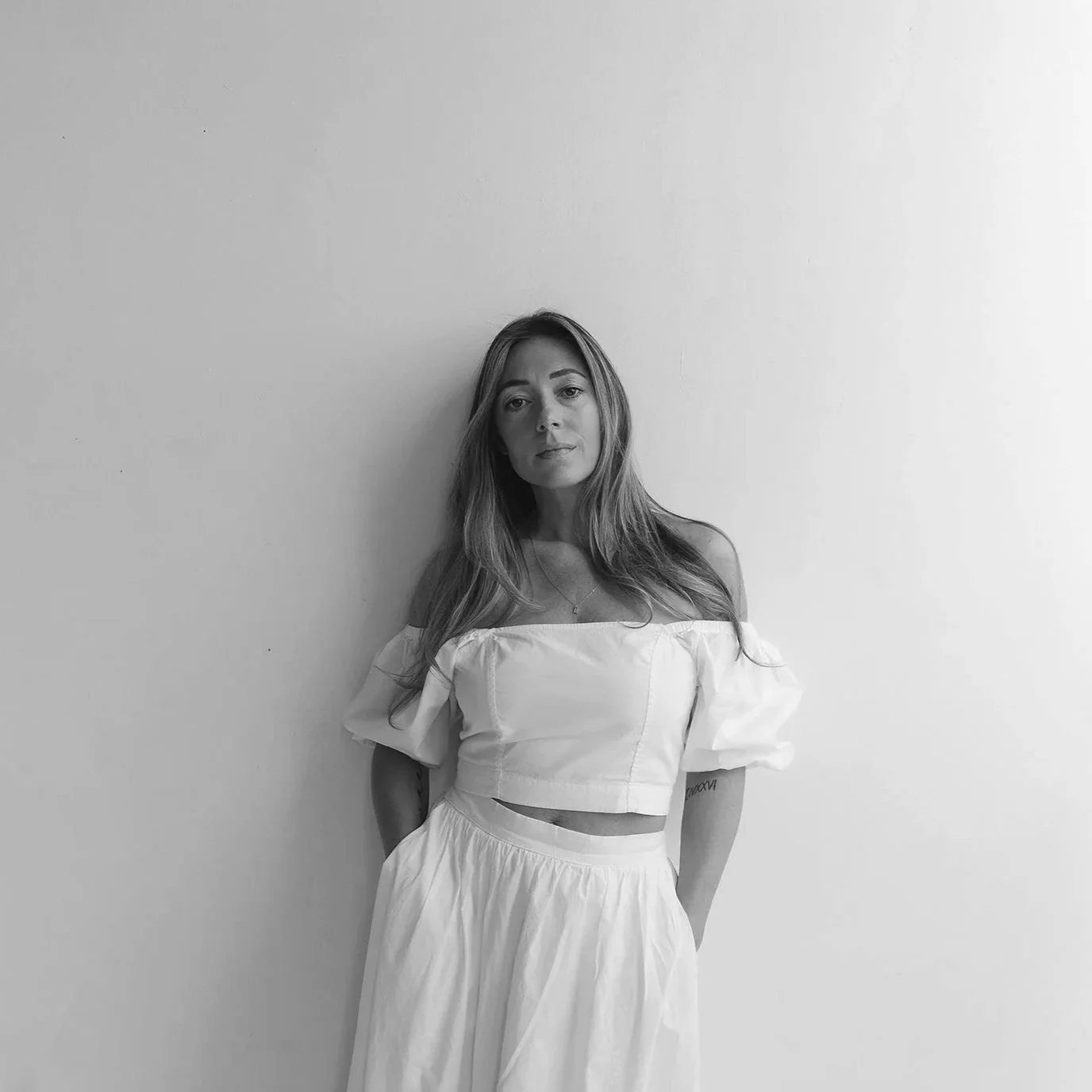A young woman with curly hair, wearing glasses, earrings, and a striped shirt, smiling in an indoor setting.