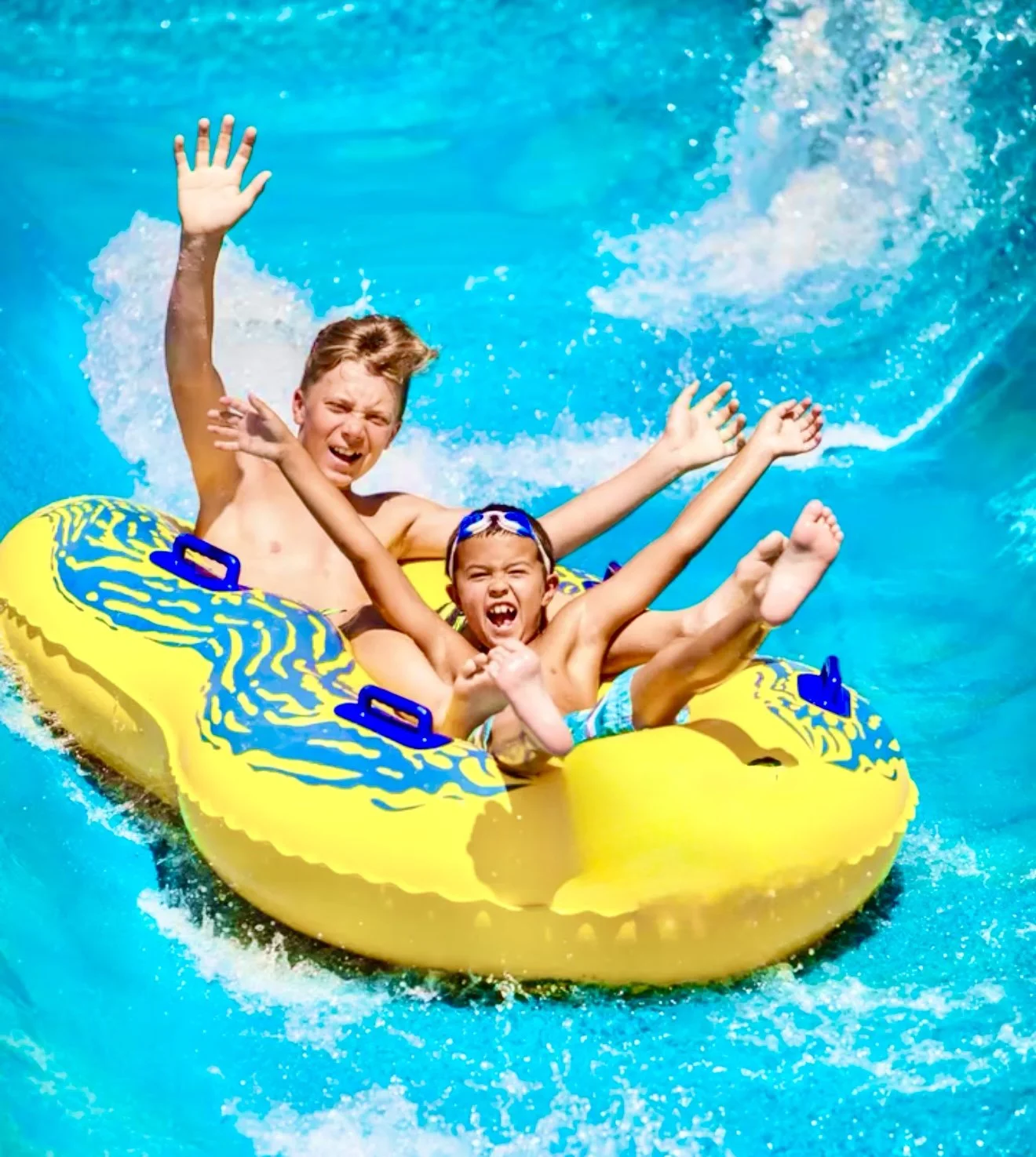 Two children, a boy and a girl, enjoying a ride on a yellow 2-person tube riding the Raging River at WaterWorks Park in Redding, CA, with water splashing around them.