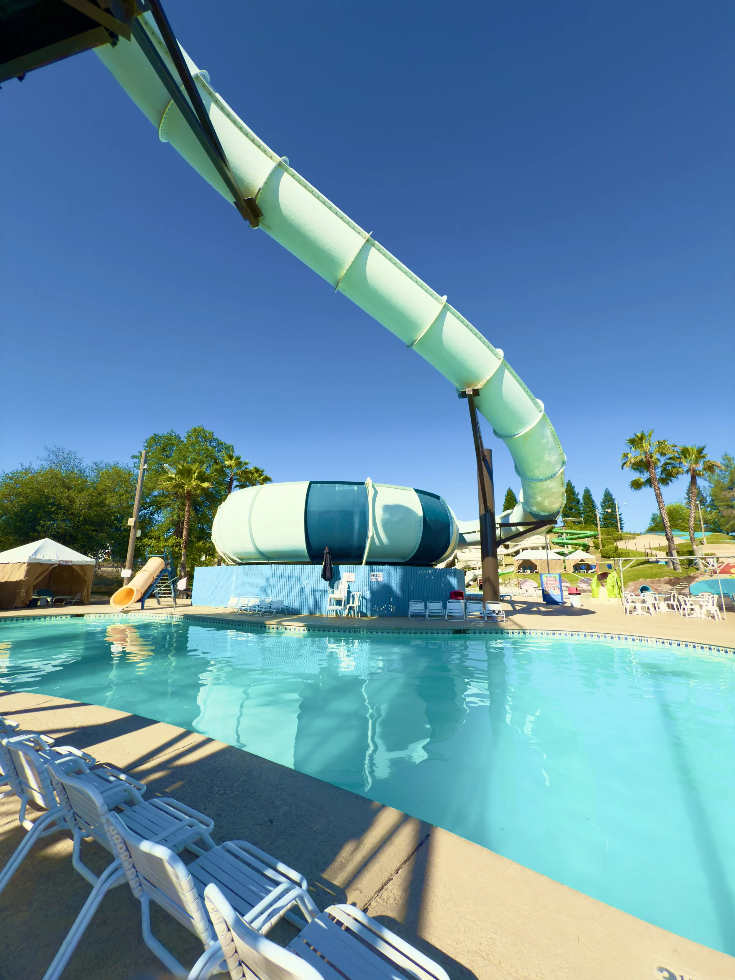 Image shows the crystal blue water Activity Pool with guest chairs bordering the sides of the pool. The Cyclone ride is featured beyond the Activity pool.