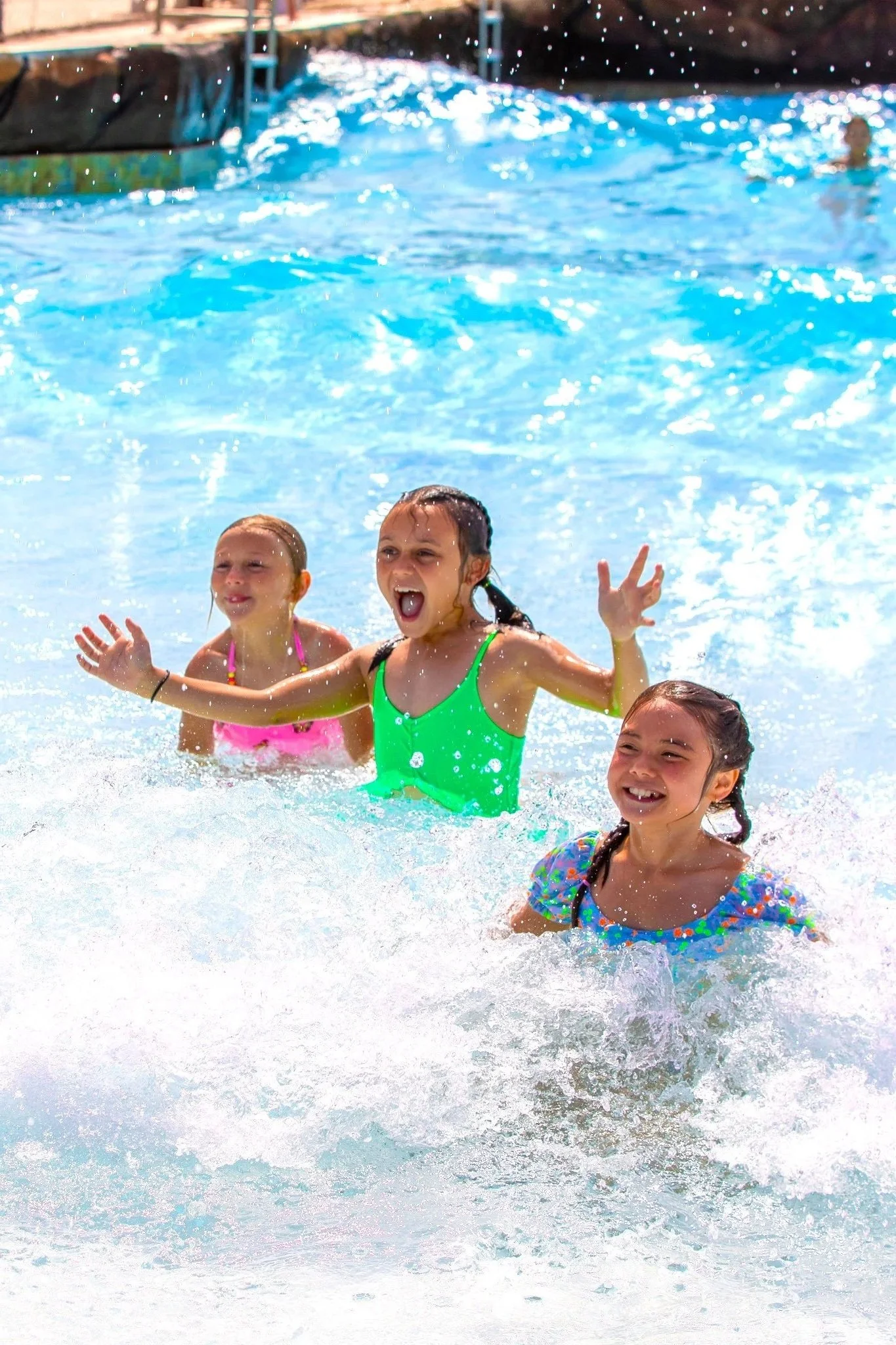 Three young girls splashing, playing and laughing in the wave pool on a sunny day. The water is crystal blue.