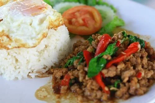Fried rice topped with a fried egg, served with a side of stir-fried ground meat with vegetables and a small salad with lettuce, tomato, and cucumber.