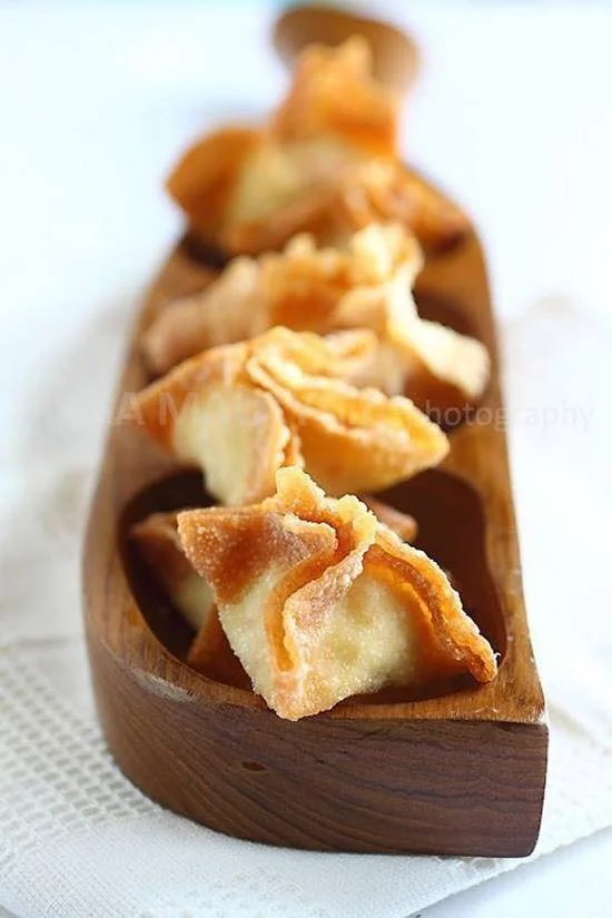 Fried wontons in a wooden serving dish on a white surface.