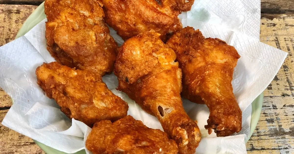 Fried chicken drumsticks on a paper towel-lined plate, placed on a wooden table.