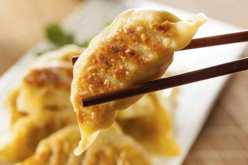 Close-up of a gyoza dumpling held by chopsticks, showing a crispy, golden-brown exterior.