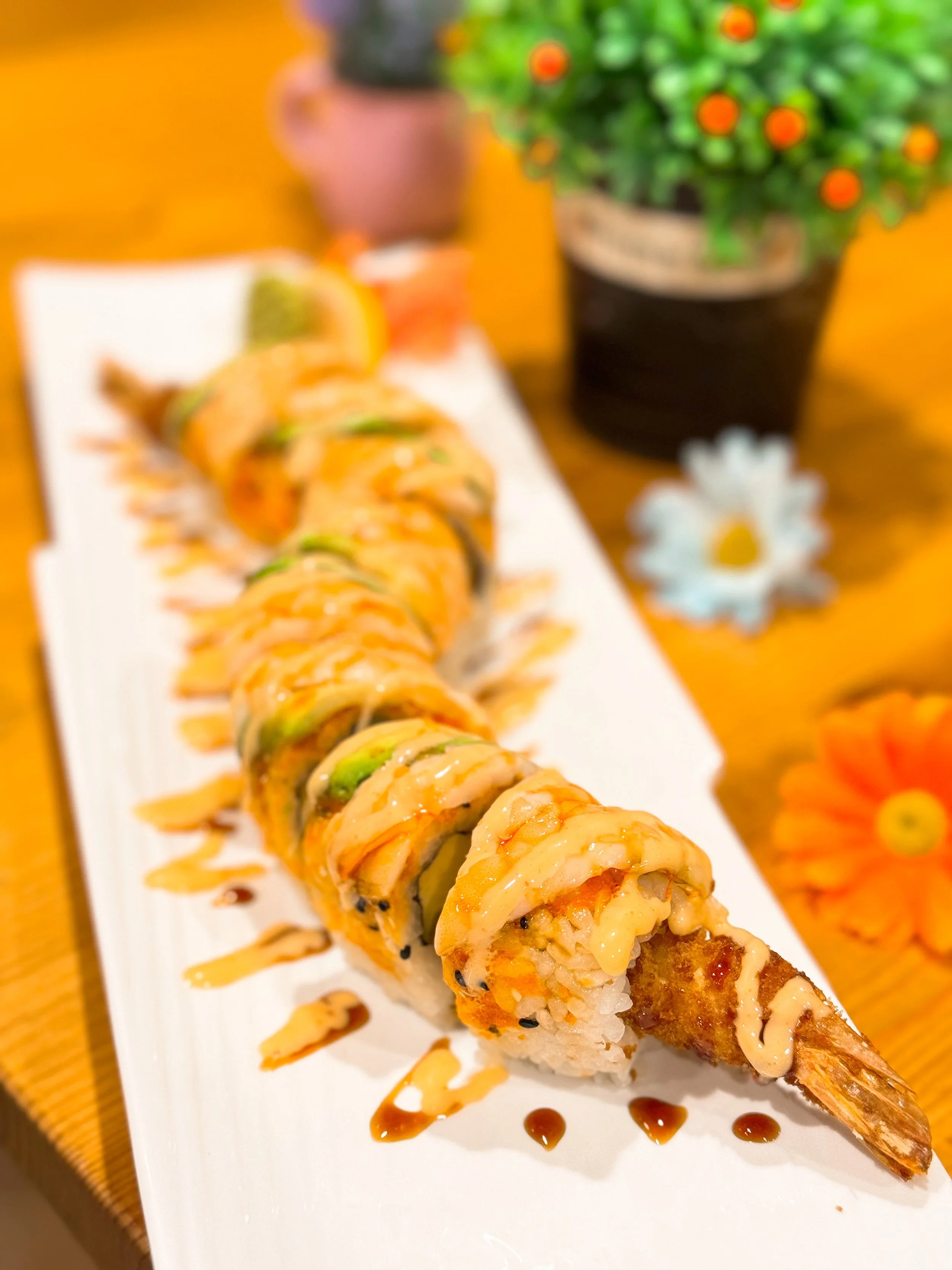 A plate of sushi rolls with eel, drizzled with sauce, placed on a white rectangular dish.