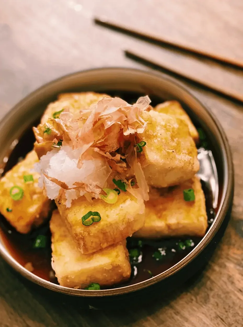 Close-up of a bowl of Japanese agedashi tofu topped with bonito flakes, chopped green onions, and grated daikon