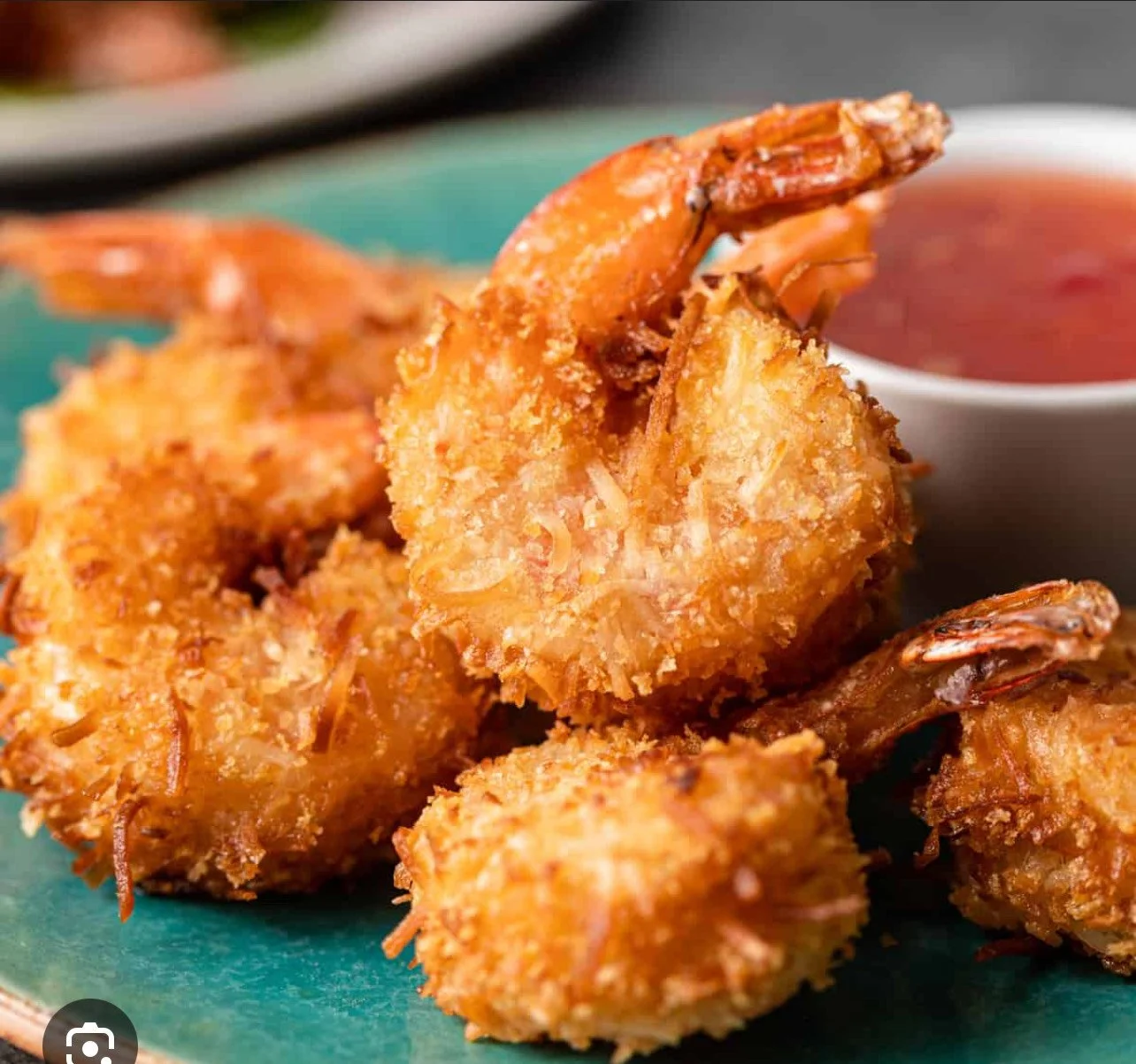 Close-up of breaded and fried shrimp on a turquoise plate with a side of red dipping sauce in a white bowl.