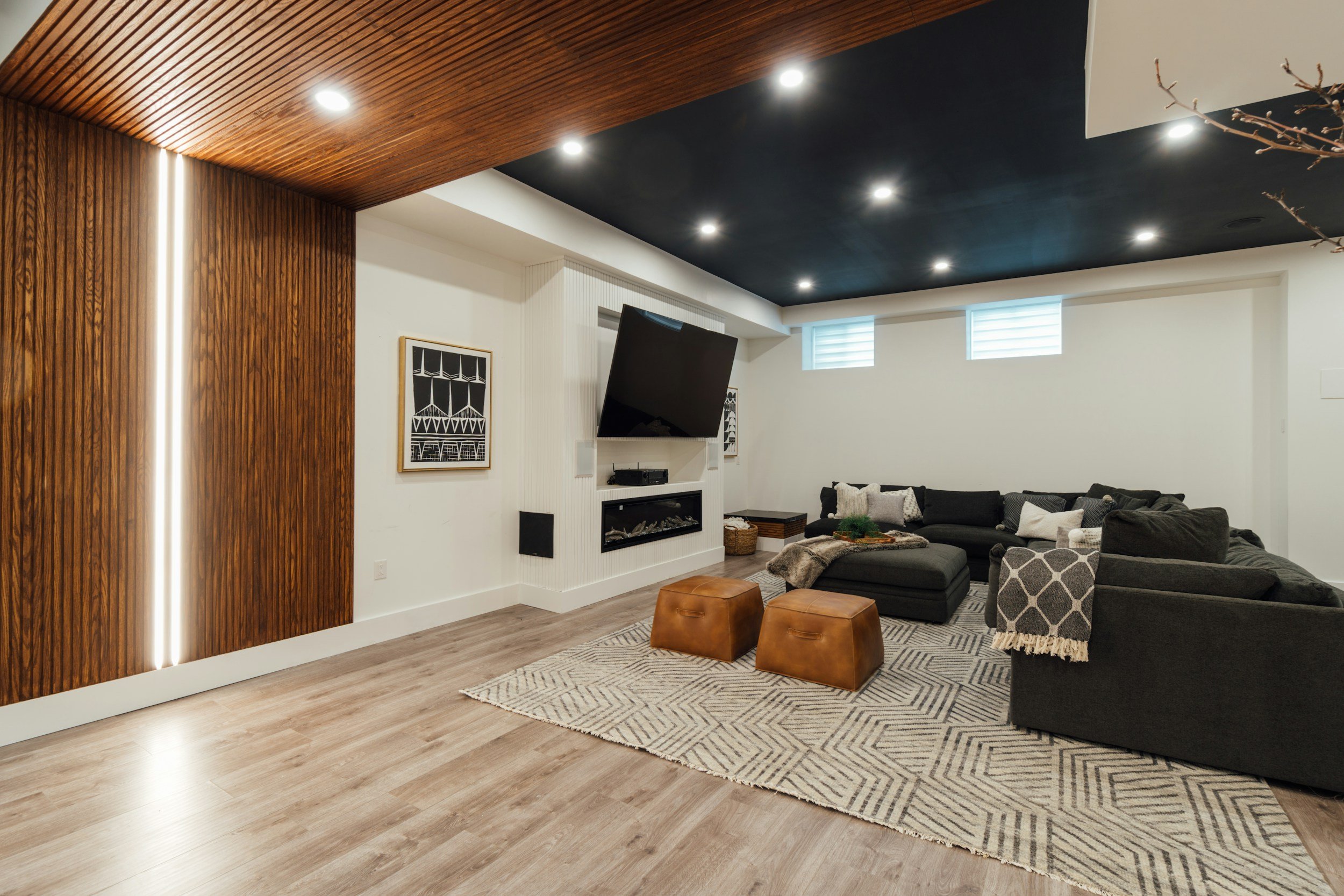 Empty finished basement with wood flooring, white walls, laundry area with washer and dryer, small bathroom with vanity, and multiple ceiling lights.