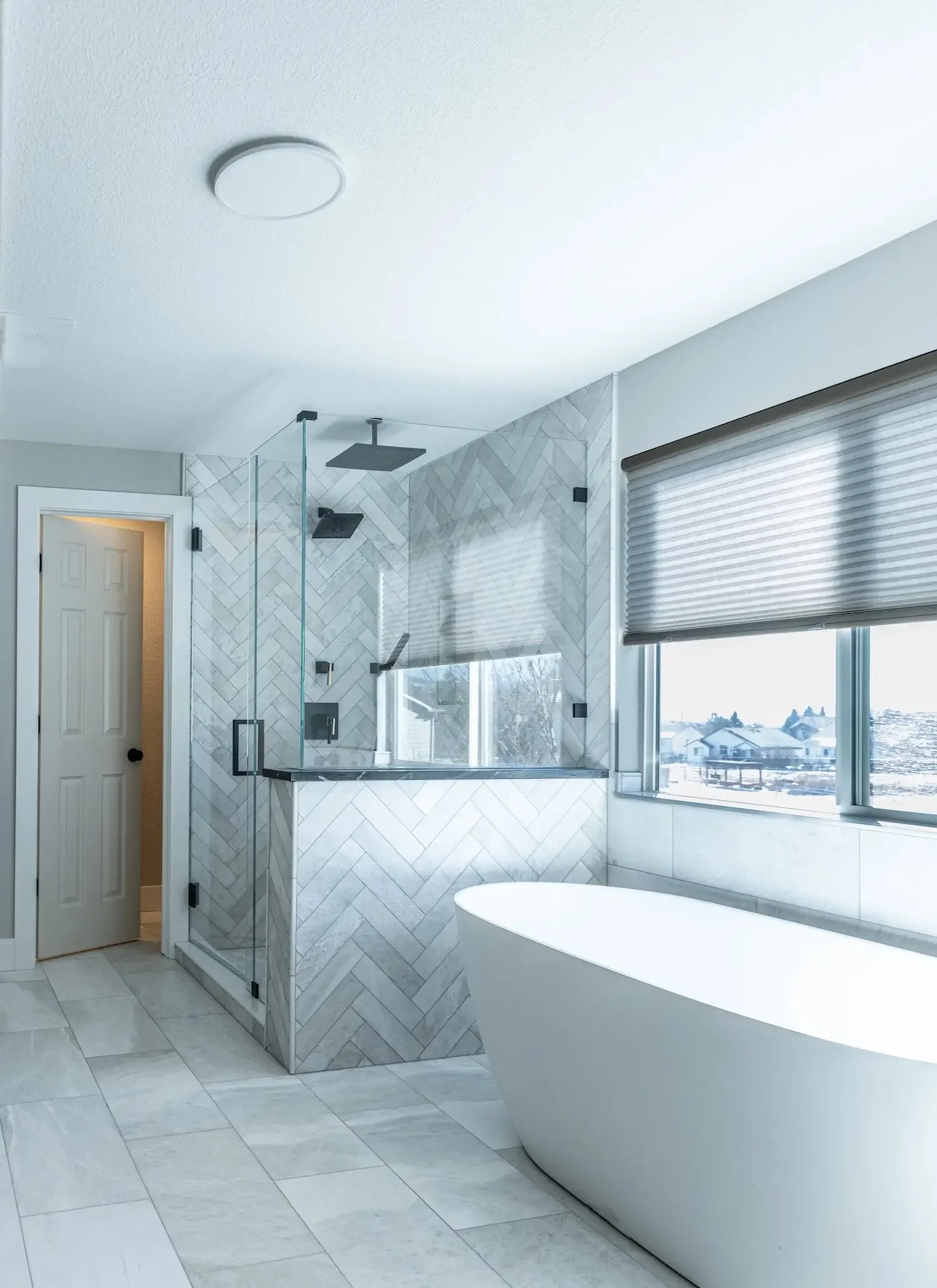 Bathroom home remodel with walk-in glass shower, gray tile walls, built-in bench, and black fixtures.