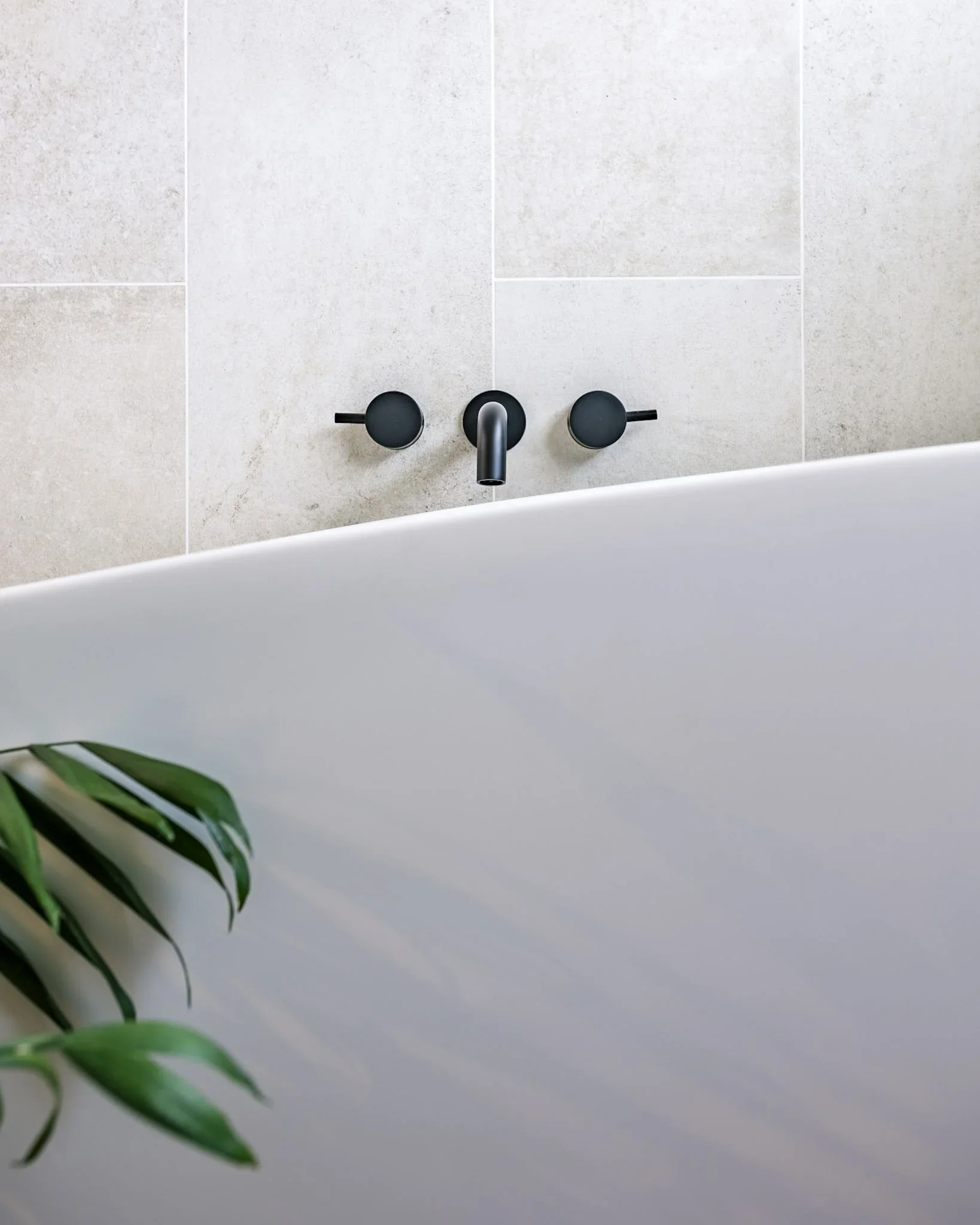 Bathroom with a black soapstone countertop, mid-century modern walnut vanity, two gold trimmed mirrors, a framed photo on the wall, a vase with purple flowers and antlers, blue towels on black towel bars, and a white door.