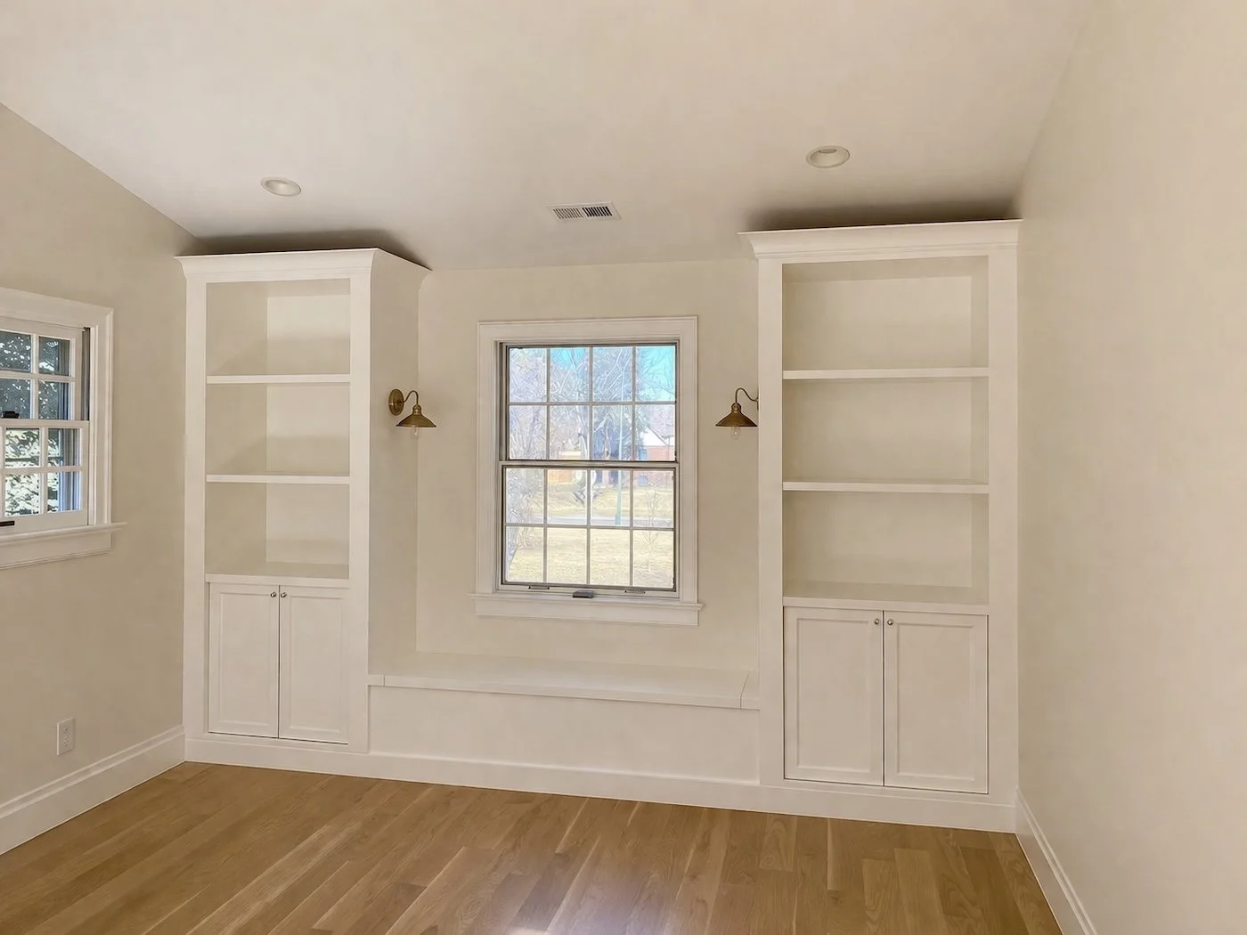 Custom white built-in shelving with window seat, cabinet bases, and brass sconces.