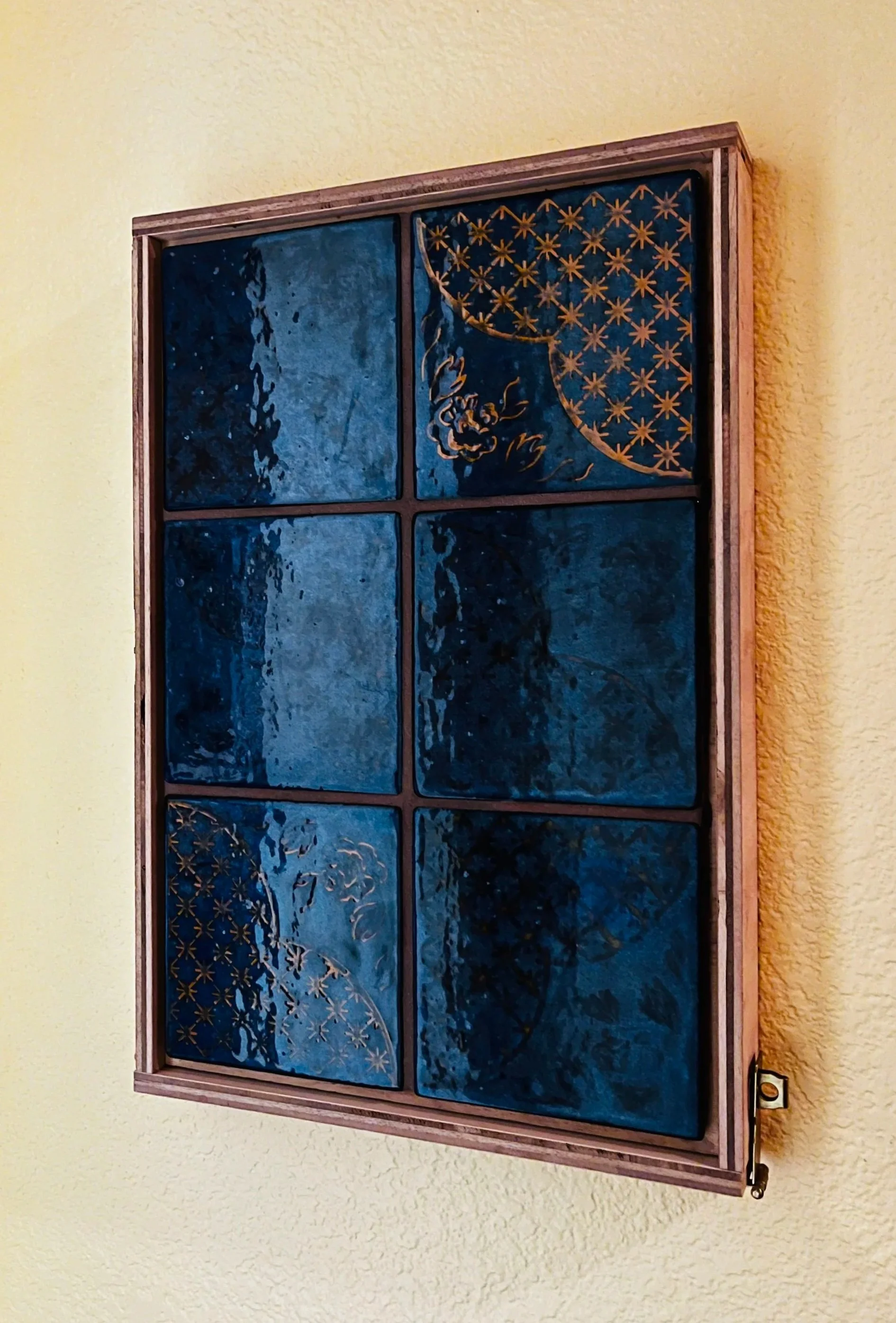 Decorative wall art featuring a grid of six blue-toned tiles with gold patterns and outlines, framed in wood, mounted on a yellow wall.