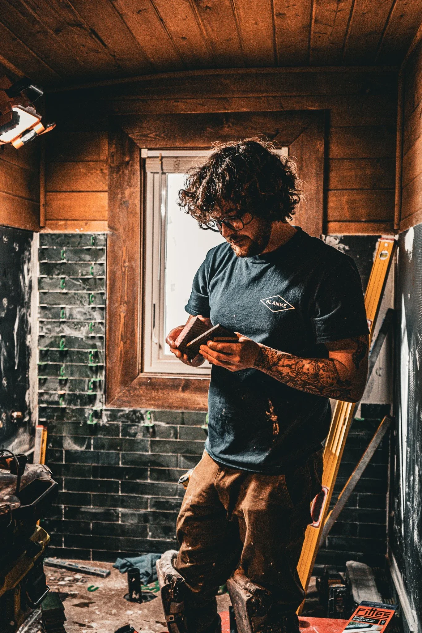 Jack Gowins, lead craftsman at Basin Design + Build examining tile on a job site in a rustic interior.