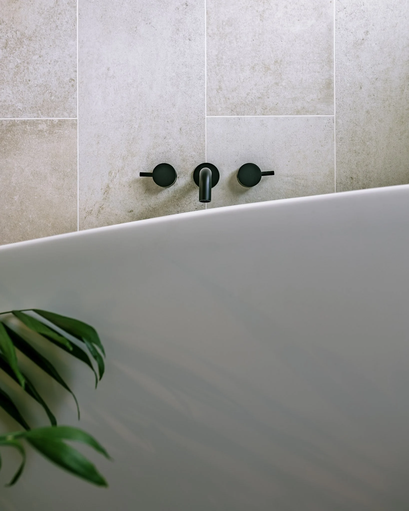 Bathroom with a black soapstone countertop, mid-century modern walnut vanity, two gold trimmed mirrors, a framed photo on the wall, a vase with purple flowers and antlers, blue towels on black towel bars, and a white door.