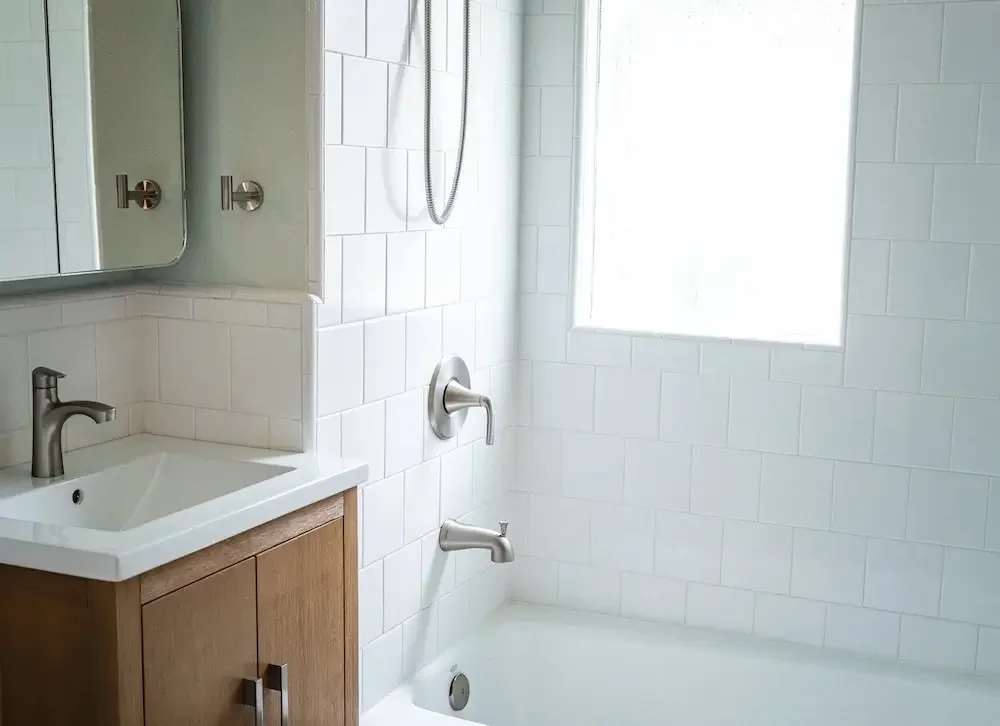 Bathroom with white tile tub surround, wood vanity, and brushed nickel fixtures