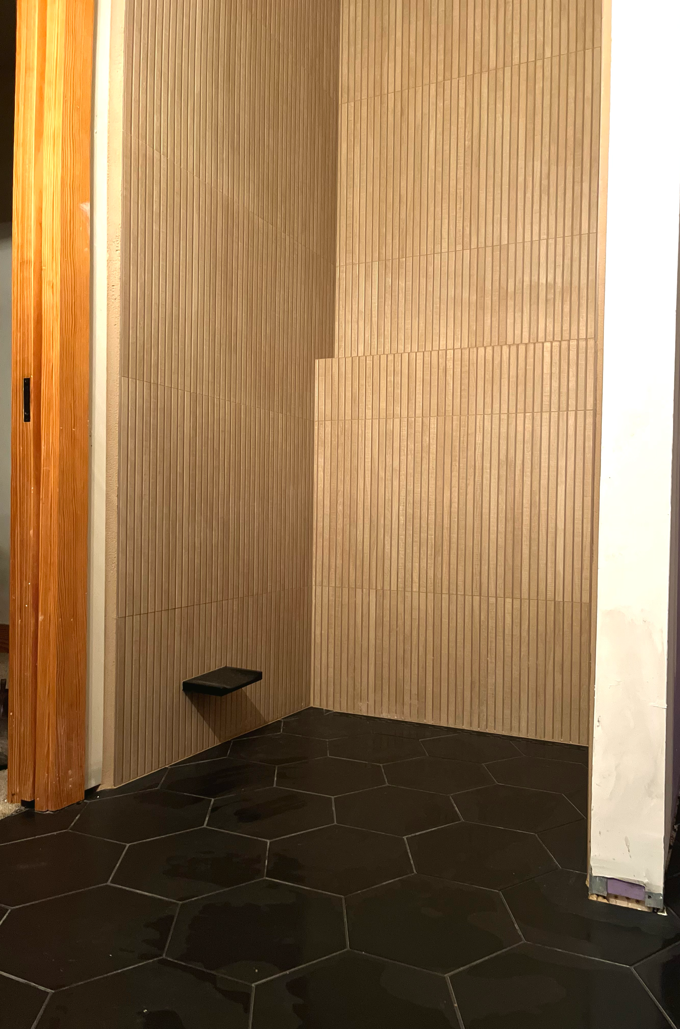 Shower with tile walls, black hexagonal floor tiles, and a small shelf on the backwall.