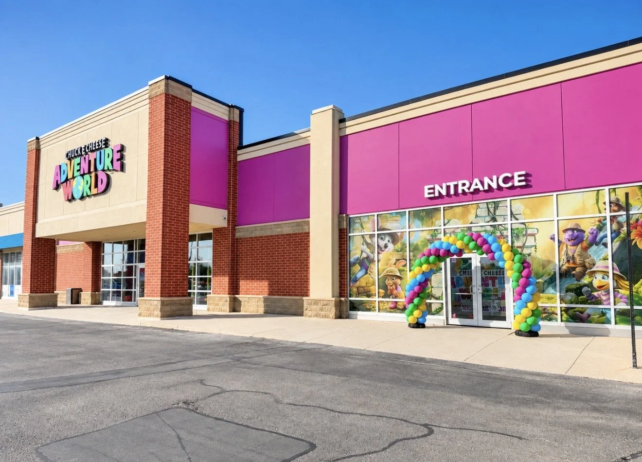 Outside view of Chuck E. Cheese Adventure World arcade with a pink and beige building, colorful balloon arch at entrance, and a glass window mural featuring animated characters from children's games.