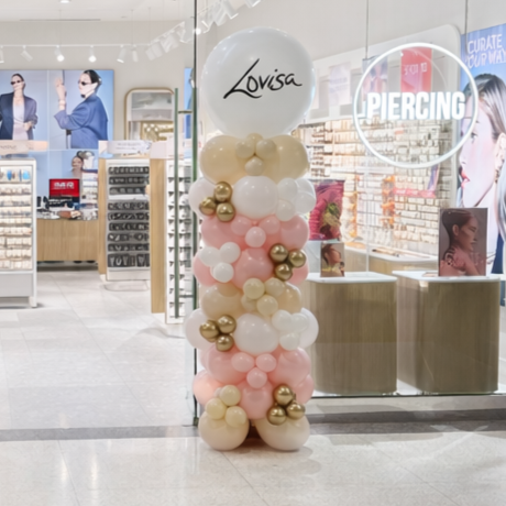 Balloon display with white, pink, and gold balloons and a large white balloon with 'Lovisa' written on it outside a jewelry store.