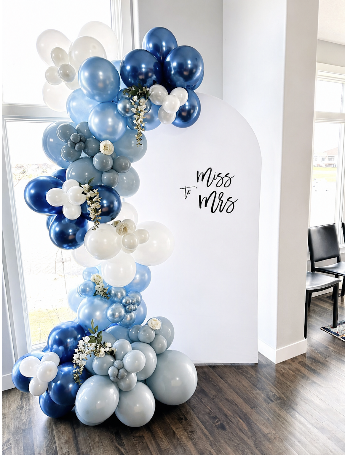Balloon arrangement with white, light blue, and dark blue balloons beside a white backdrop that has black cursive text reading 'Miss to Mrs' for a celebration event.