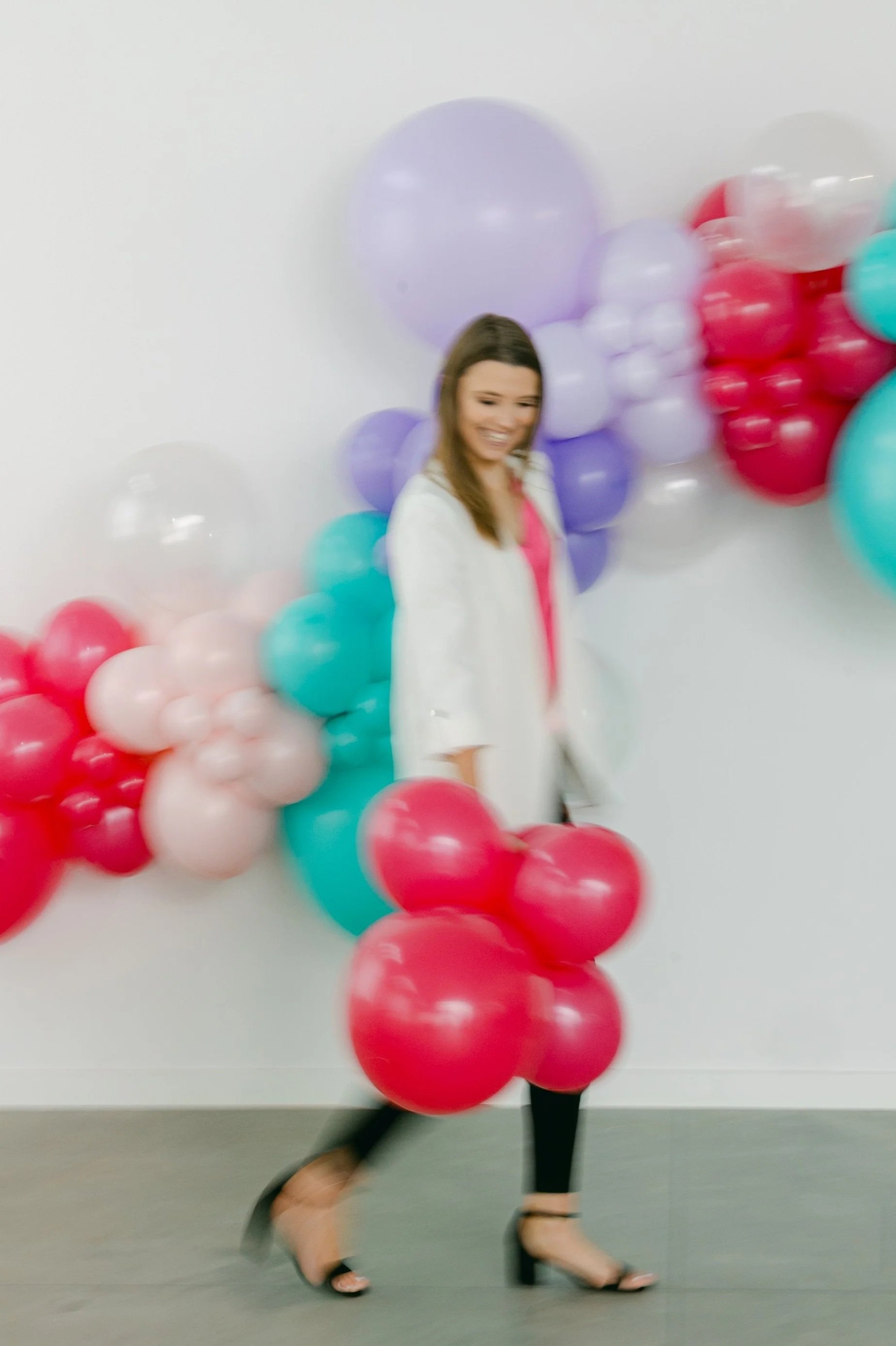 Woman standing in front of a colorful balloon display with purple, pink, red, peach, and teal balloons