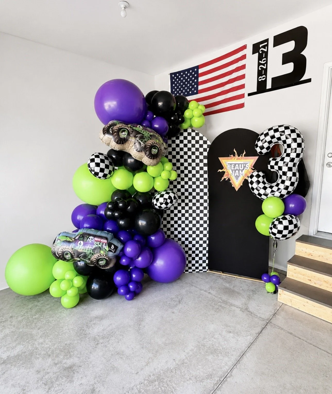 Balloon decoration with purple, green, black, and checkered pattern balloons, American flag, and a black backdrop with the logo 'Beau's Jam' for a birthday celebration. Monster Truck Birthday Party Fargo