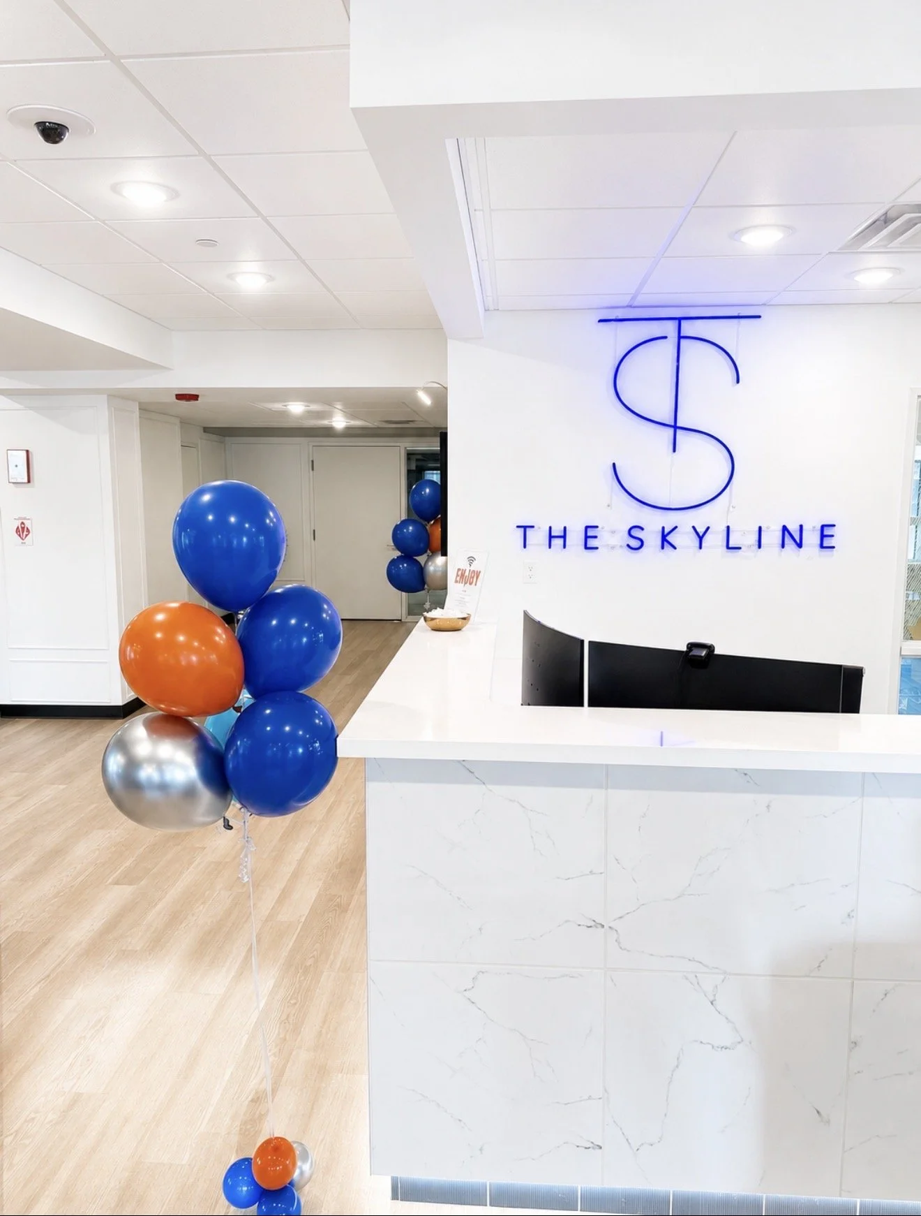 Lobby reception area with a sign reading "The Skyline" and a cluster of blue, orange, and silver balloons.