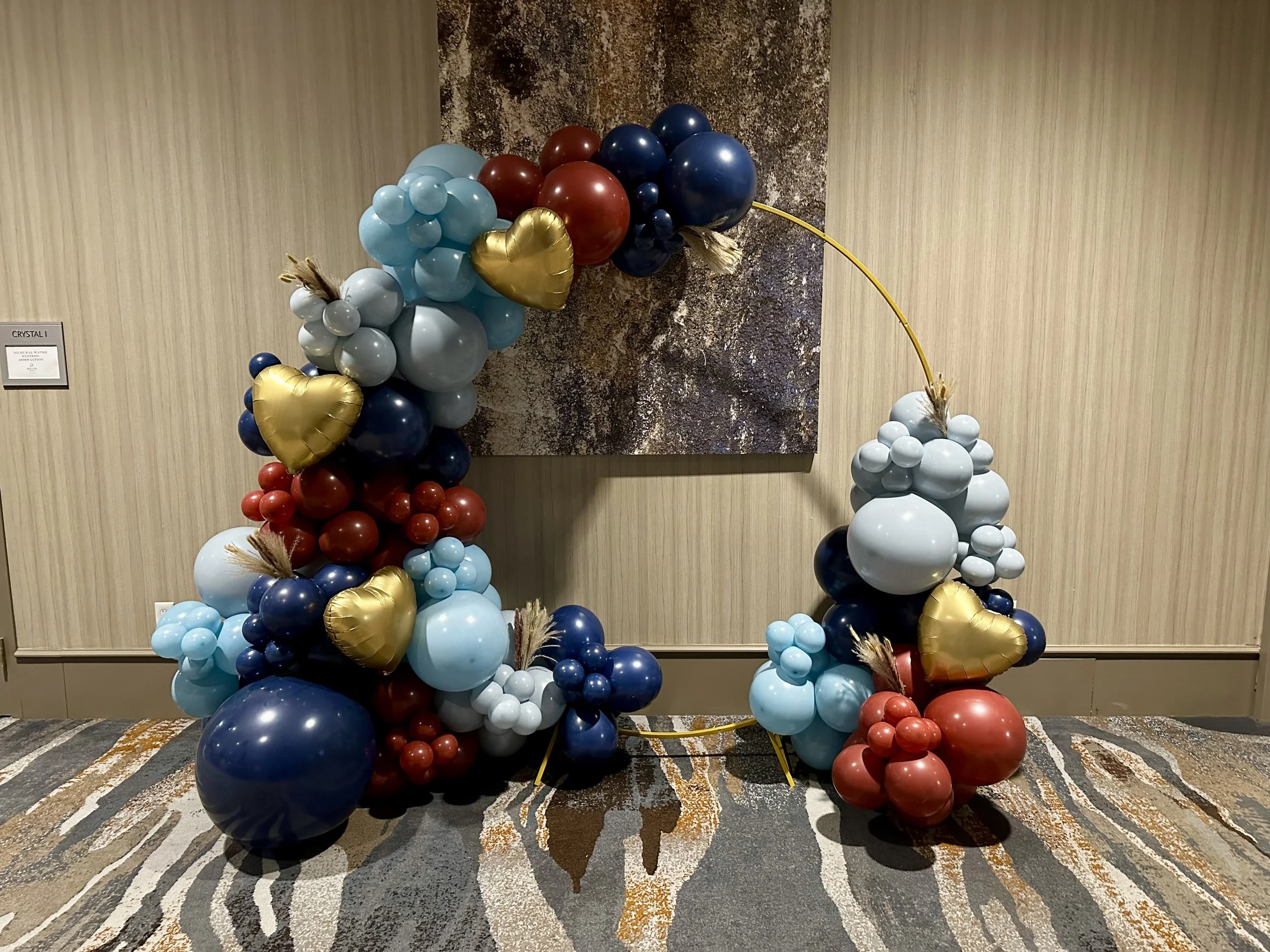Balloon arch with red, blue, light blue, gray, and gold balloons, decorated for the Ronald McDonald House Charities of the Red River Valley Sweetheart Ball
