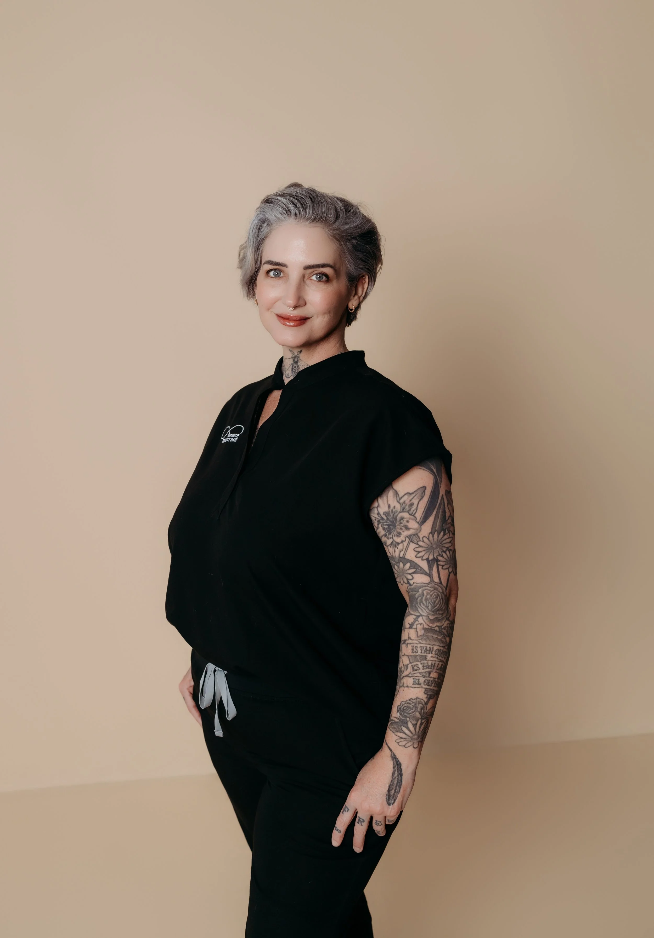 Infinite Beauty Bar's licensed esthetician Stephanie has platinum blonde hair, as well as a septum piercing and tattoos visible on her neck.