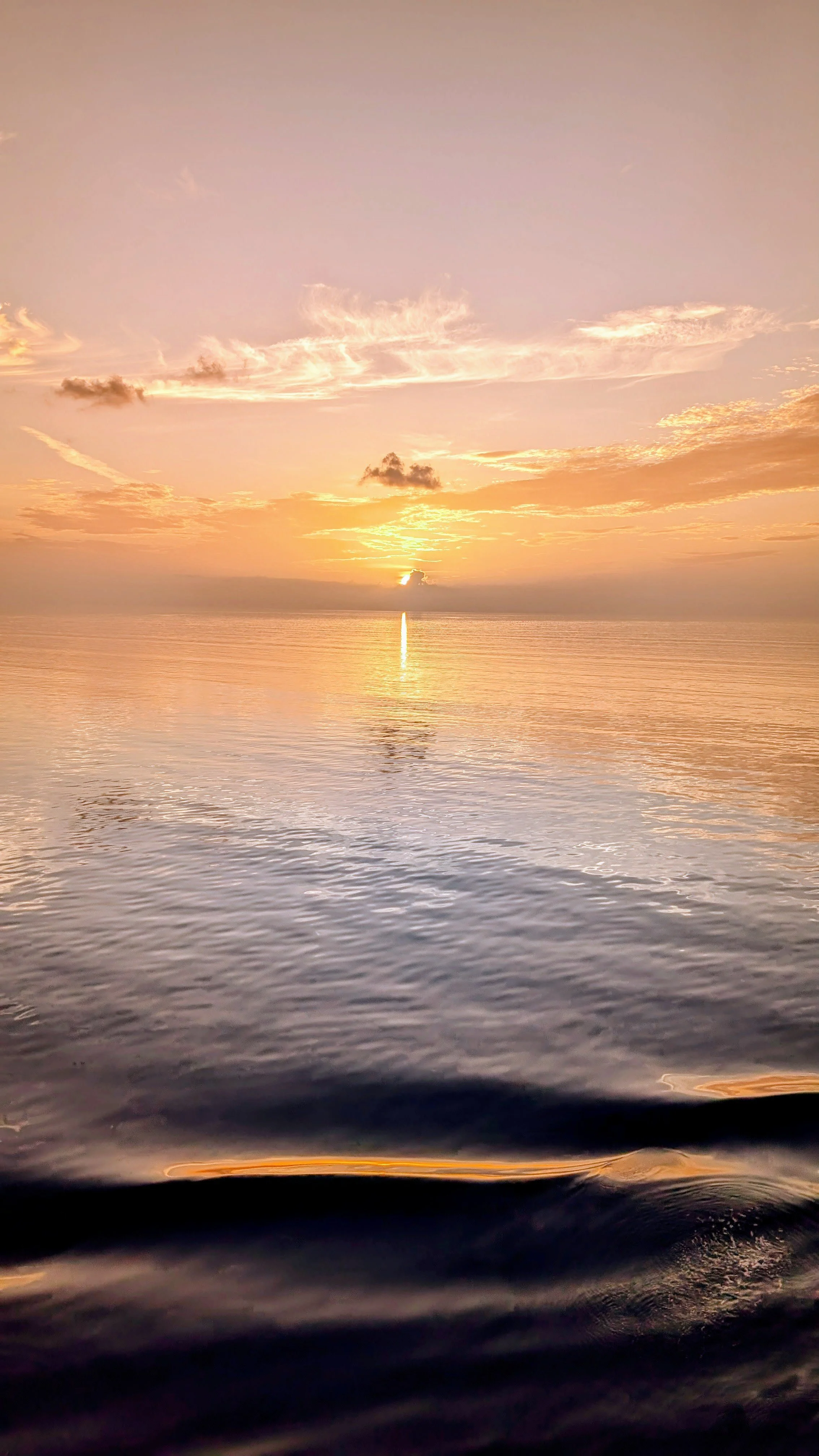 A sunset over a calm ocean with colorful sky and a reflection of the sun on the water.