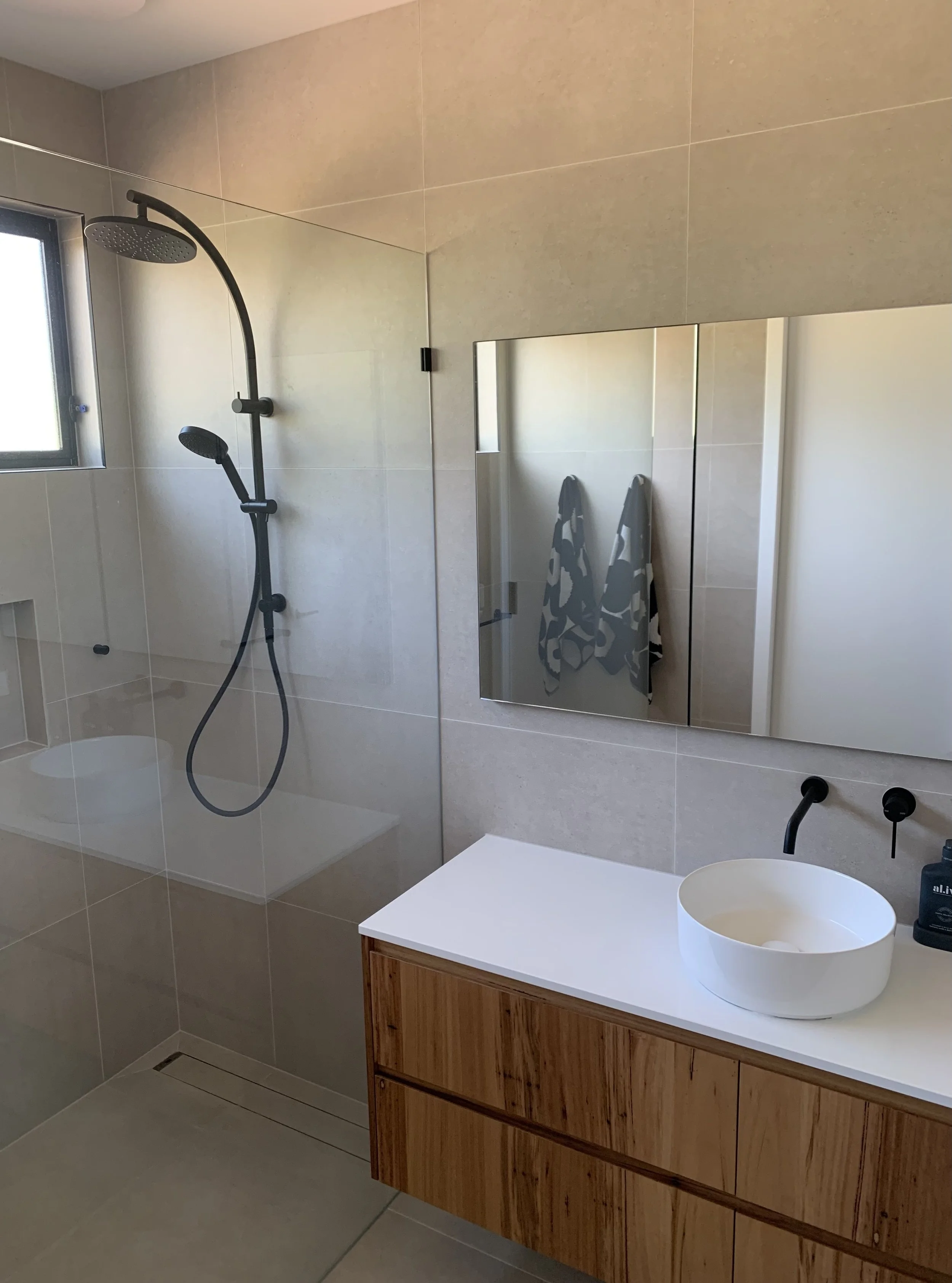 Bathroom Renovation – Wangaratta. A modern bathroom renovation featuring a blackbutt wall-hung vanity with a Caesarstone benchtop, complemented by full-height tiling and a recessed mirrored cabinet for added storage.