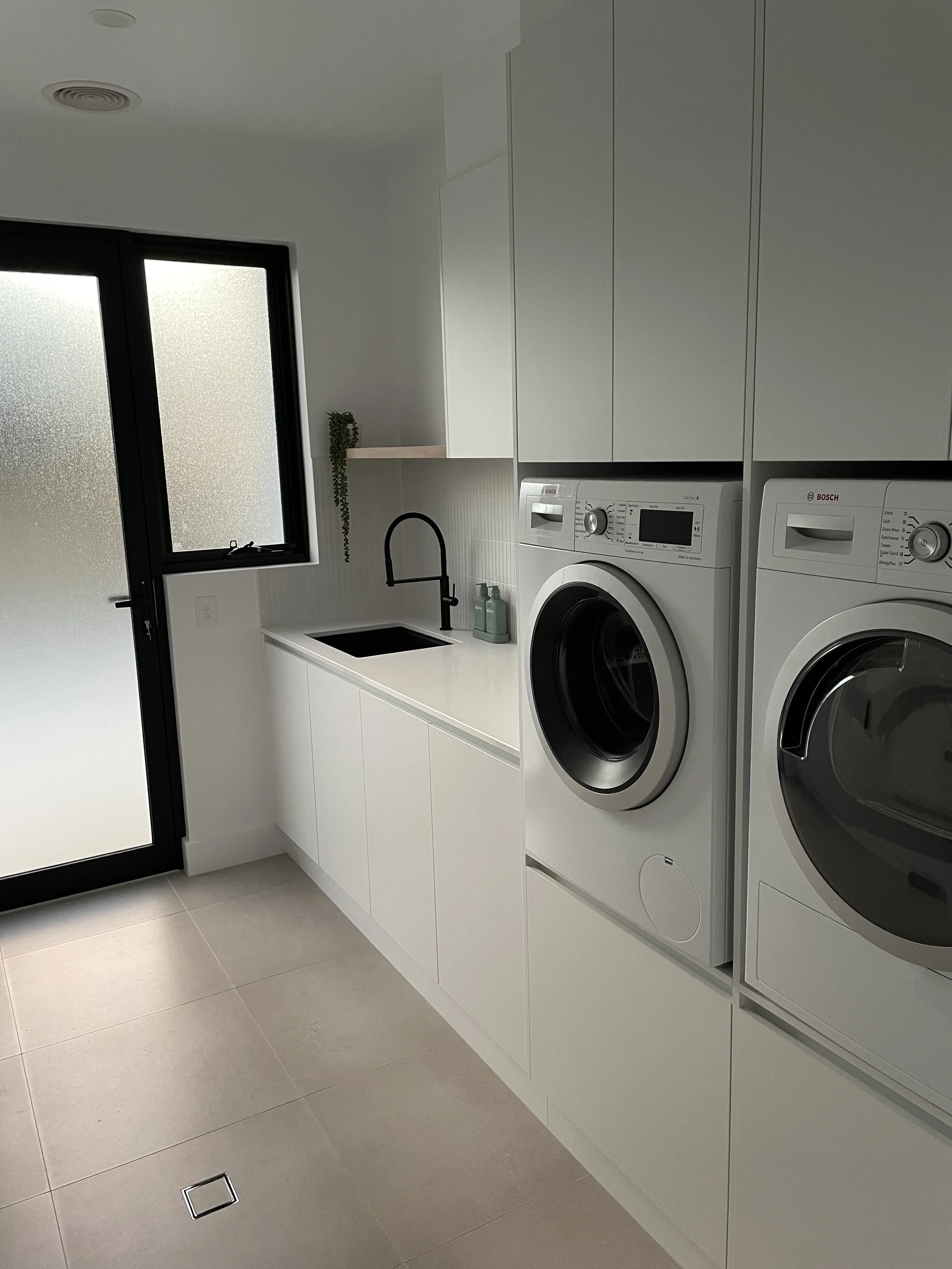 Laundry Renovation – Wangaratta. A custom laundry designed for everyday ease, featuring raised appliances, integrated storage drawers, and a stone benchtop with an undermount sink.