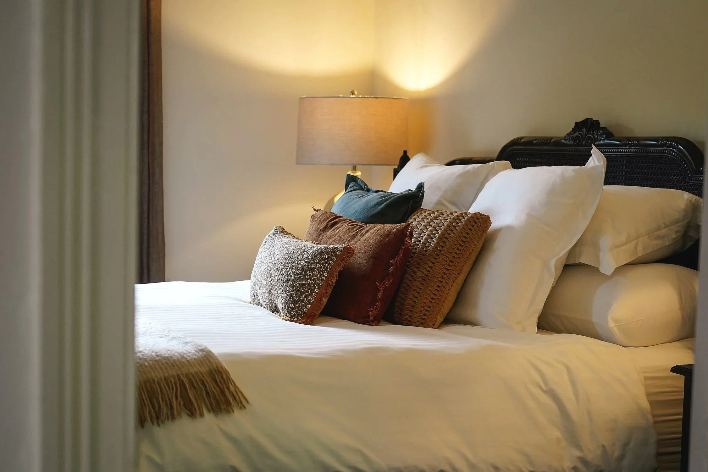 A neatly made bed with multiple decorative pillows and a lamp on the nightstand in a cozy bedroom.