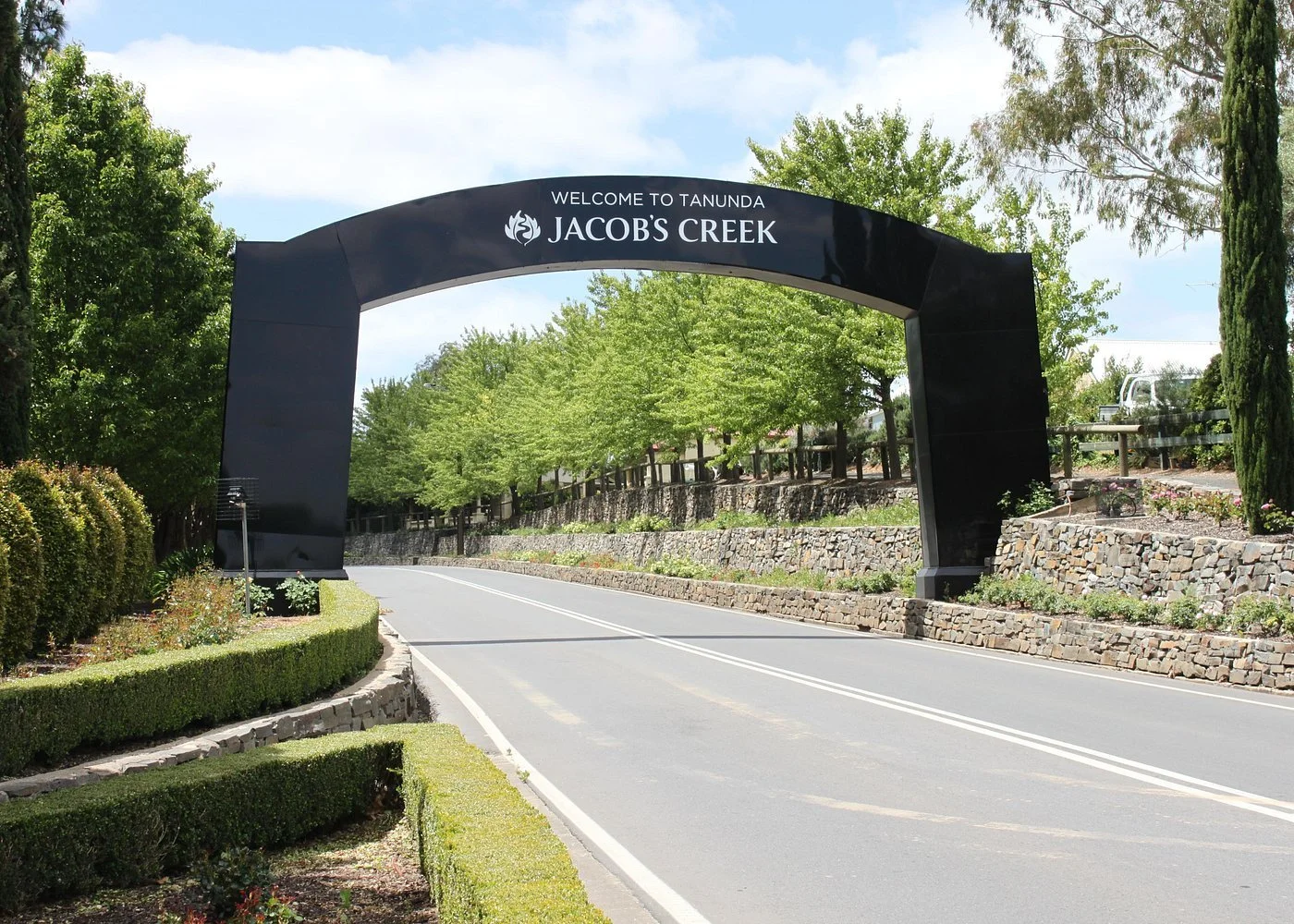 Entrance archway reading 'Welcome to Tanunda Jacob's Creek' over a road lined with trees and shrubs.